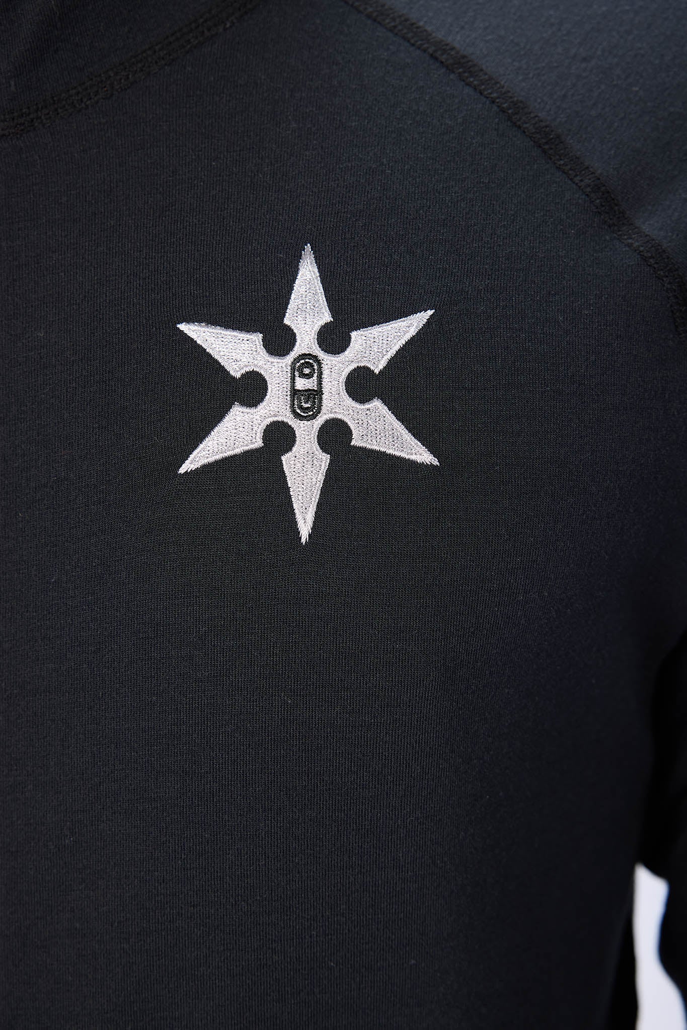 Close-up of a black long-sleeve athletic top featuring a white six-pointed star logo with a small black rectangular emblem in the center, on the chest.