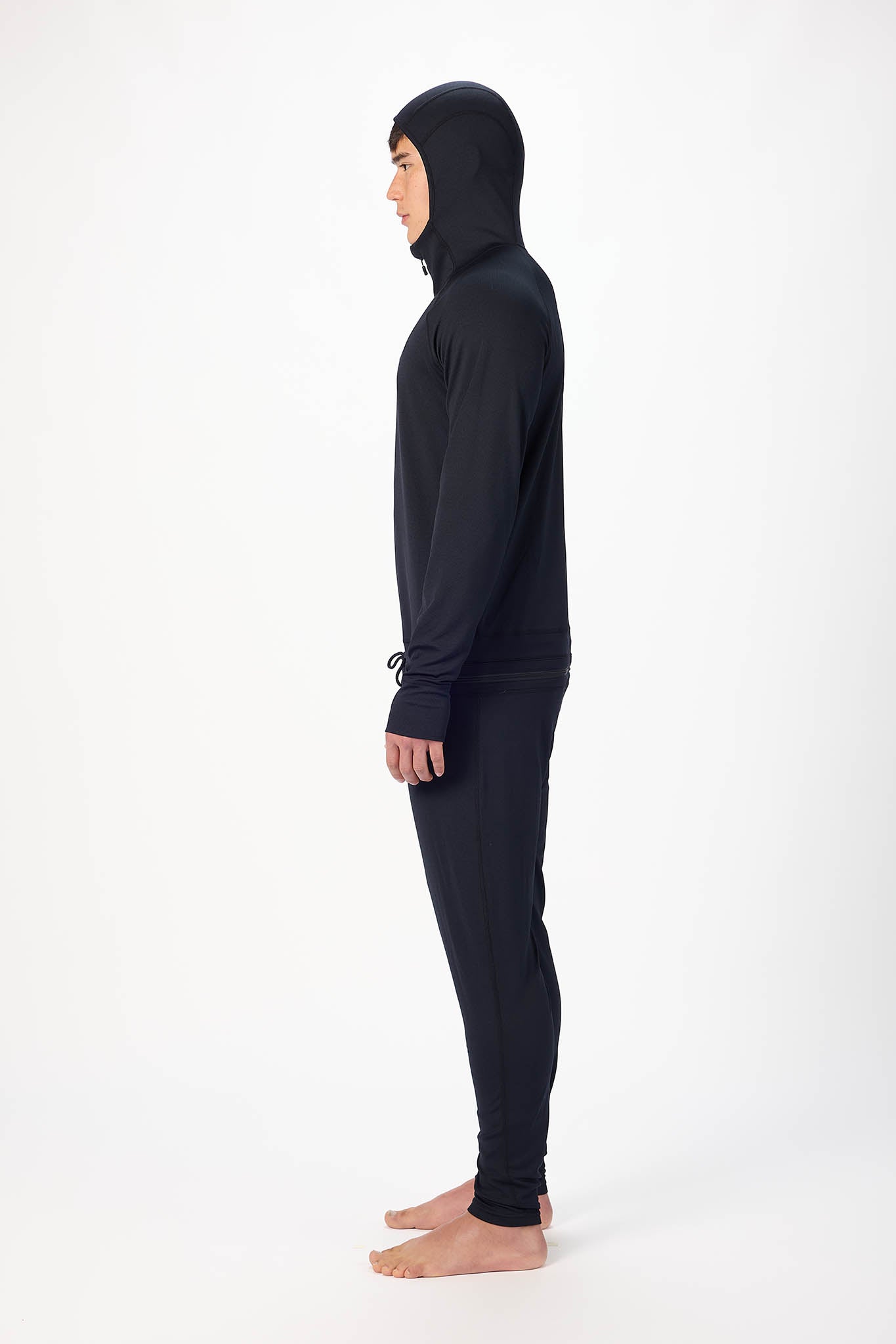 side profile A man wearing a Olive  onesie with a hooded with a zipper and jogger pants, standing against a plain white studio background.