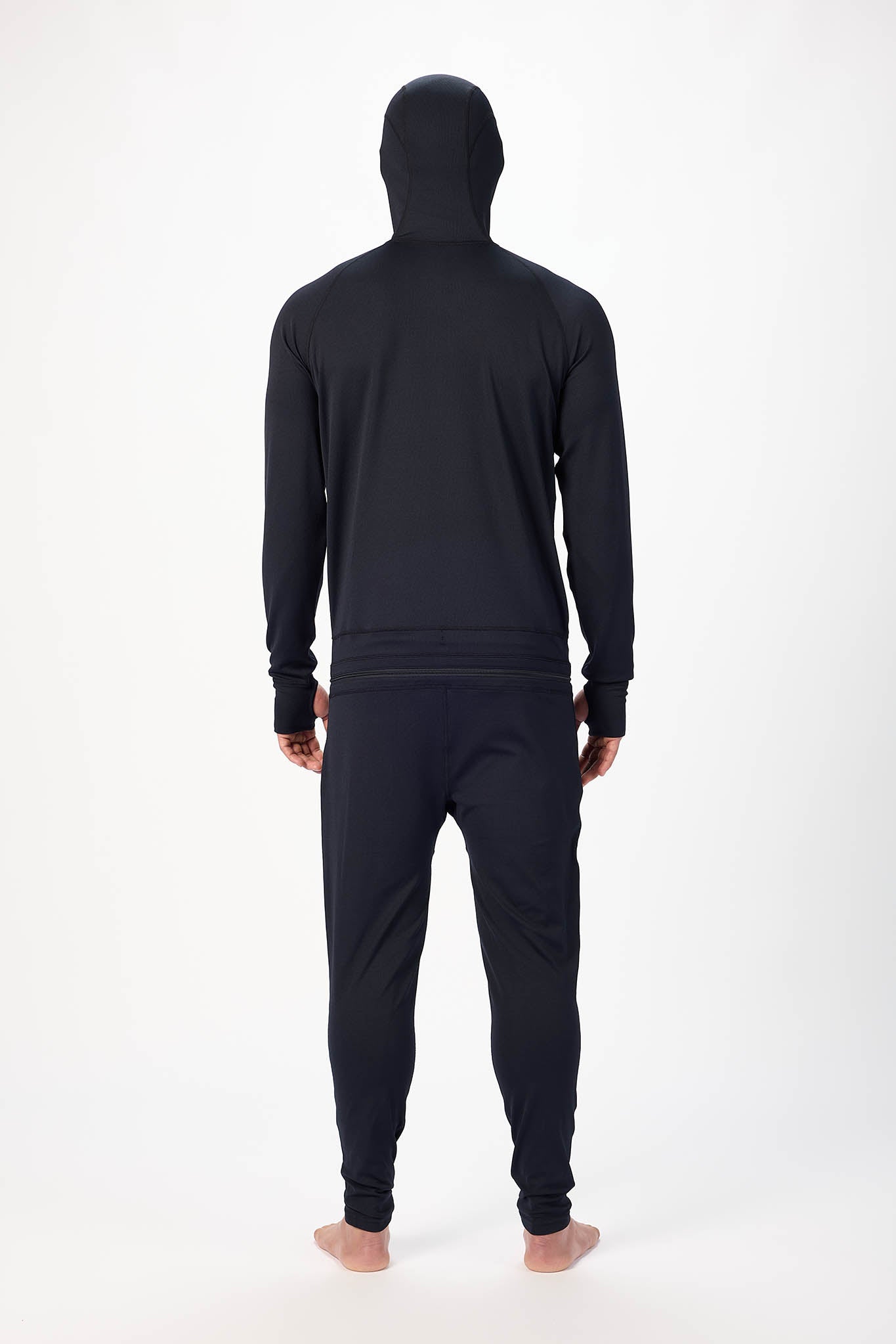 view of behind A man wearing a Olive  onesie with a hooded with a zipper and jogger pants, standing against a plain white studio background.