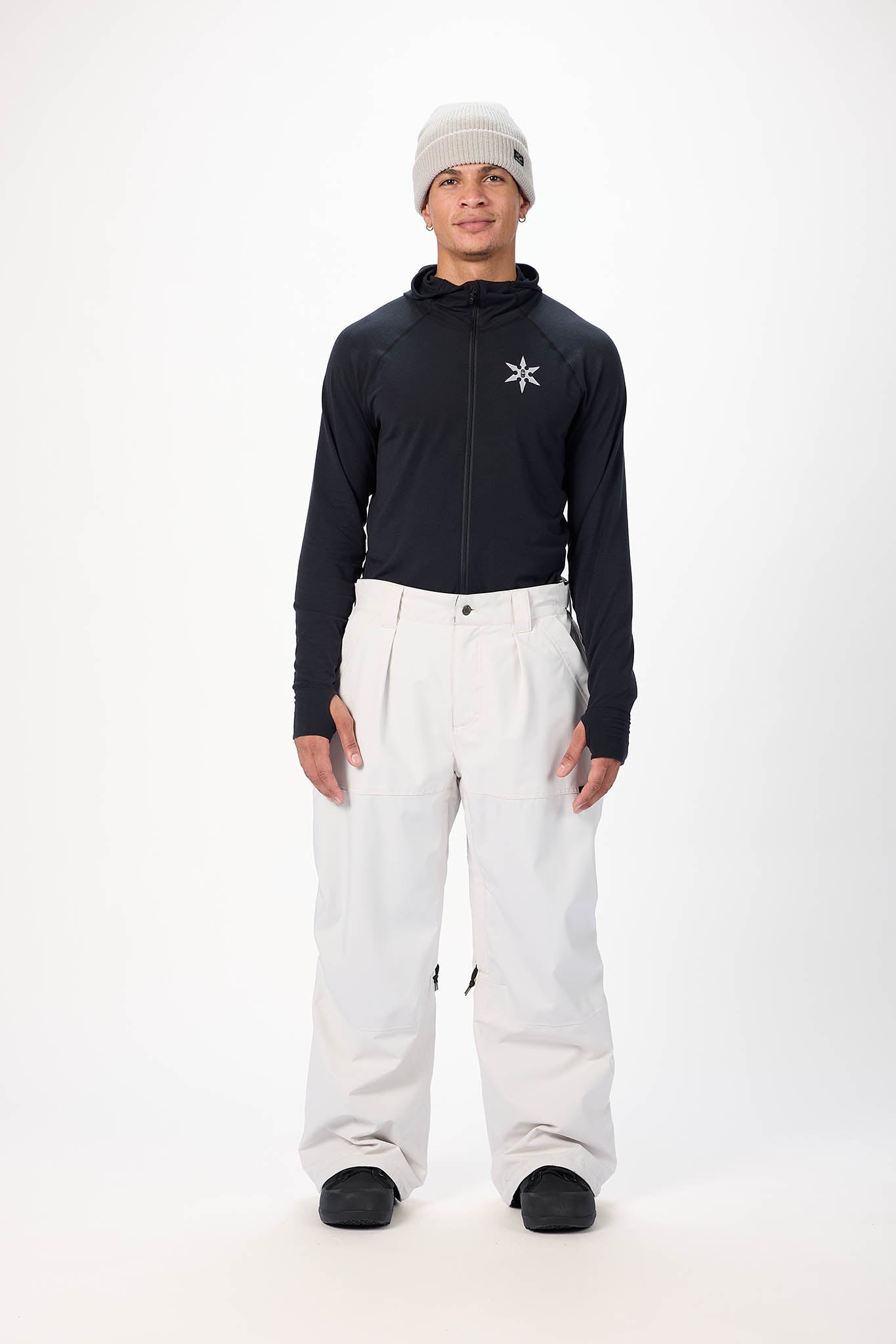 Person wearing a black jacket, white pants, and a beanie on a white background