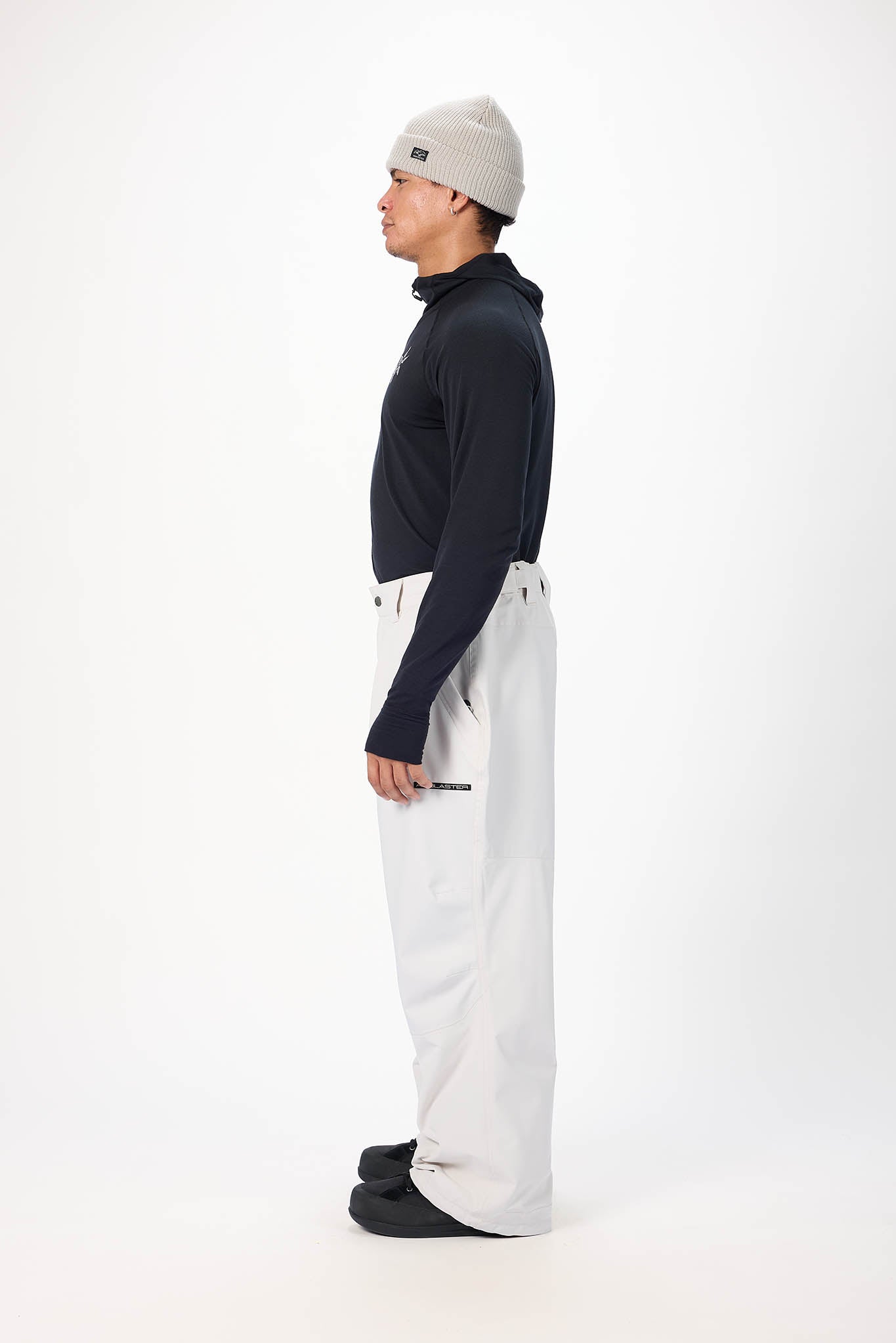 Person wearing a navy turtleneck, white pants, and a gray beanie on a white background
