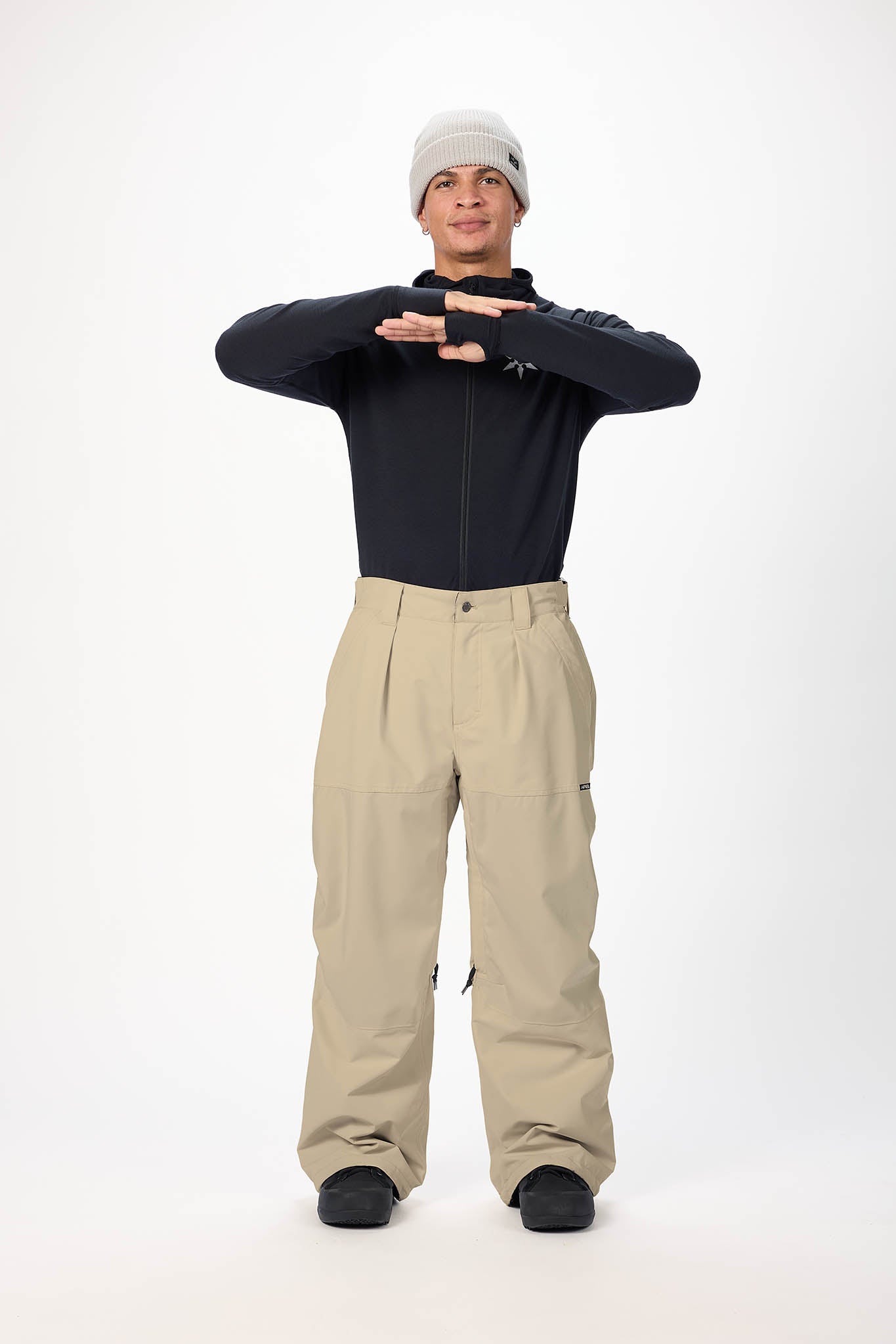 Person wearing a black jacket and beige pants on a white background