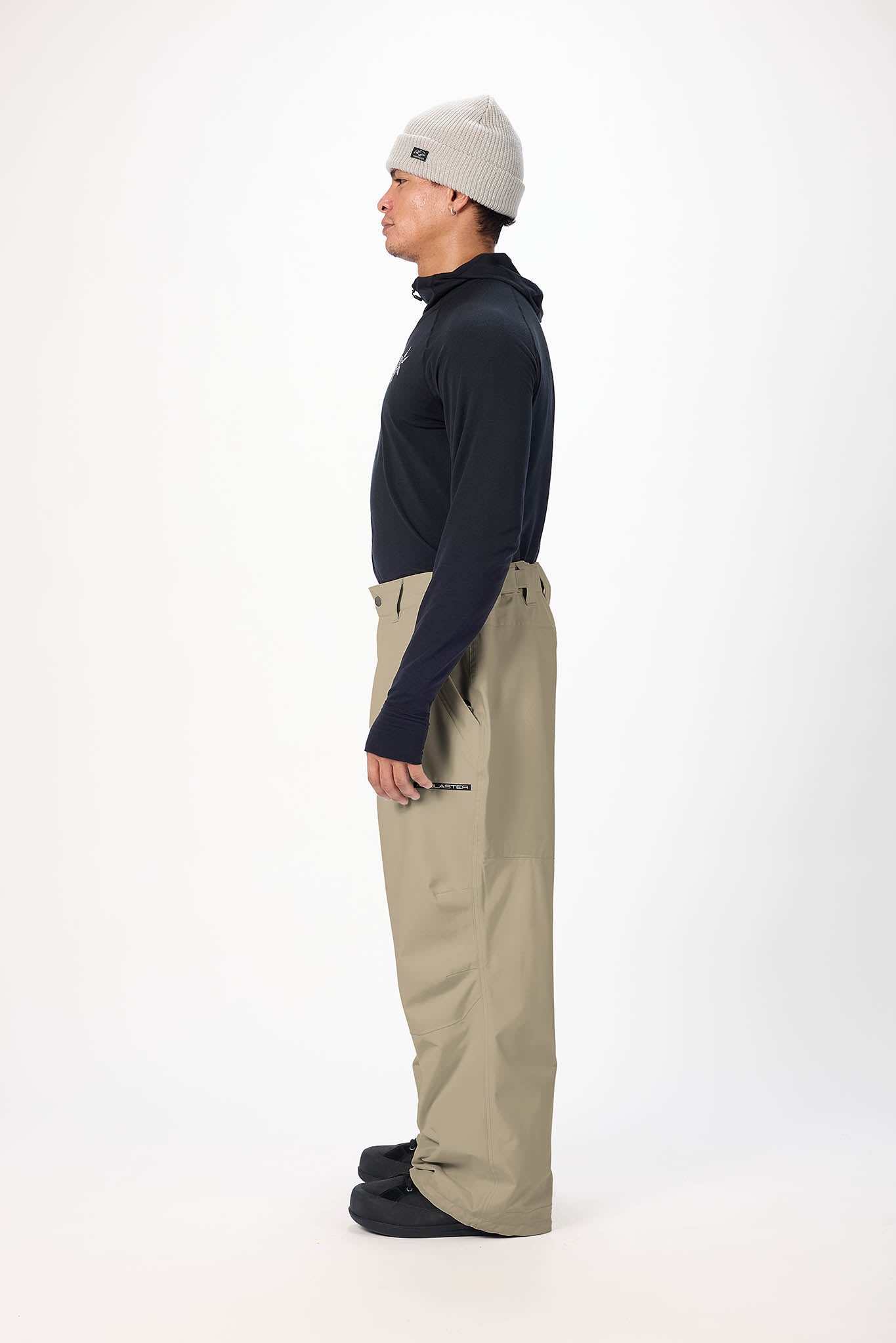 Person wearing a navy long-sleeve shirt, beige pants, and a beige beanie on a white background
