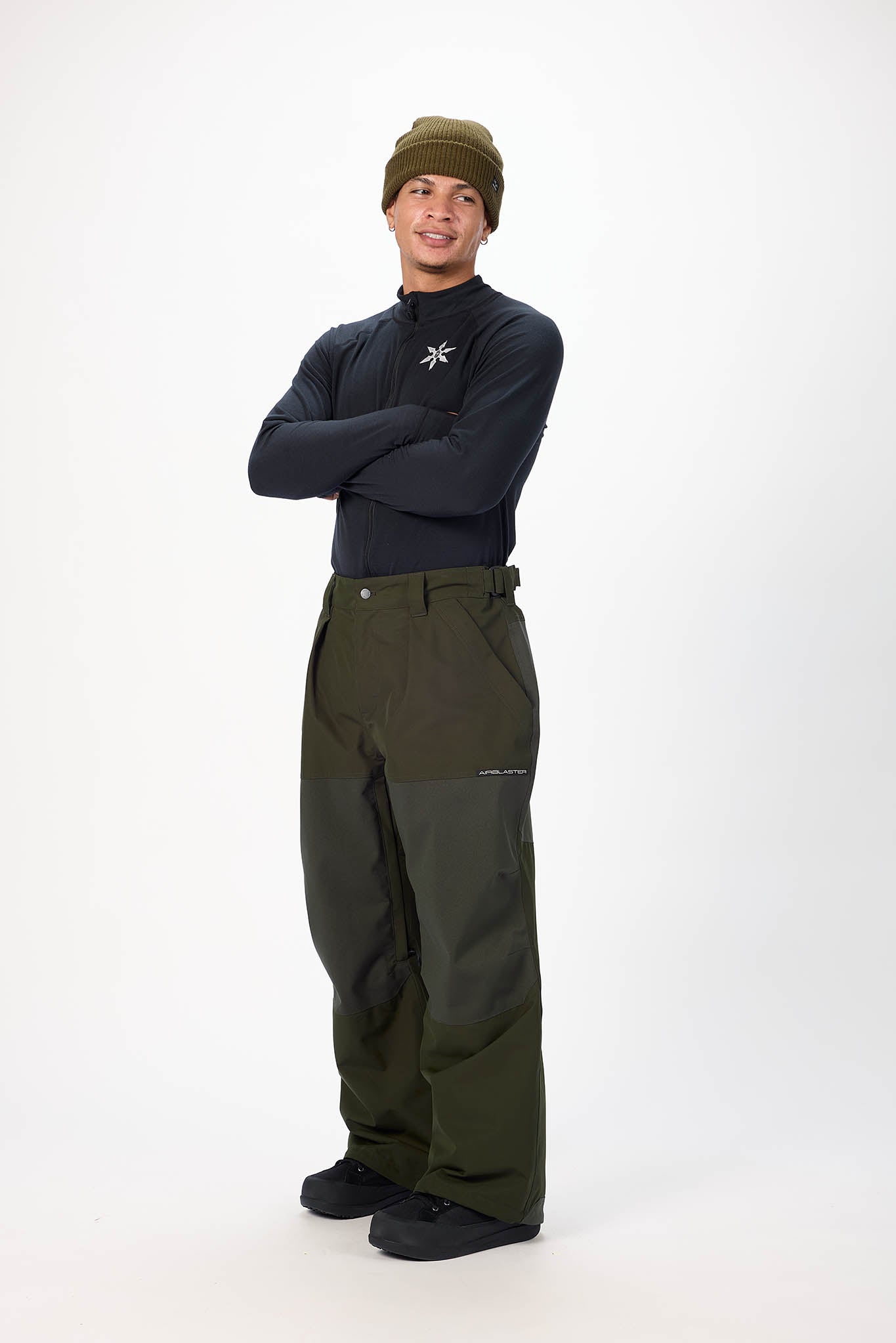 Person wearing a dark jacket, green pants, and a beanie on a white background