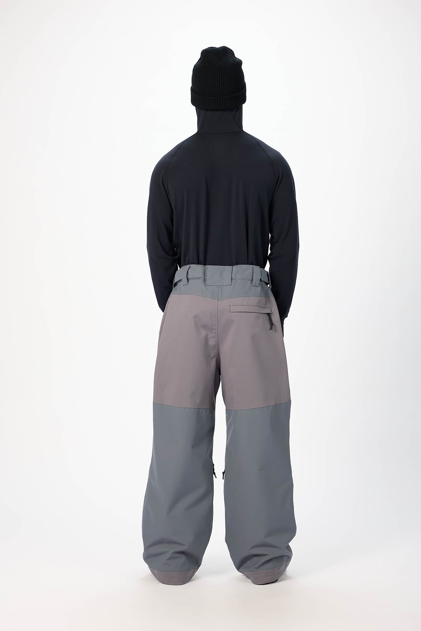 Person wearing a black jacket and gray pants on a white background