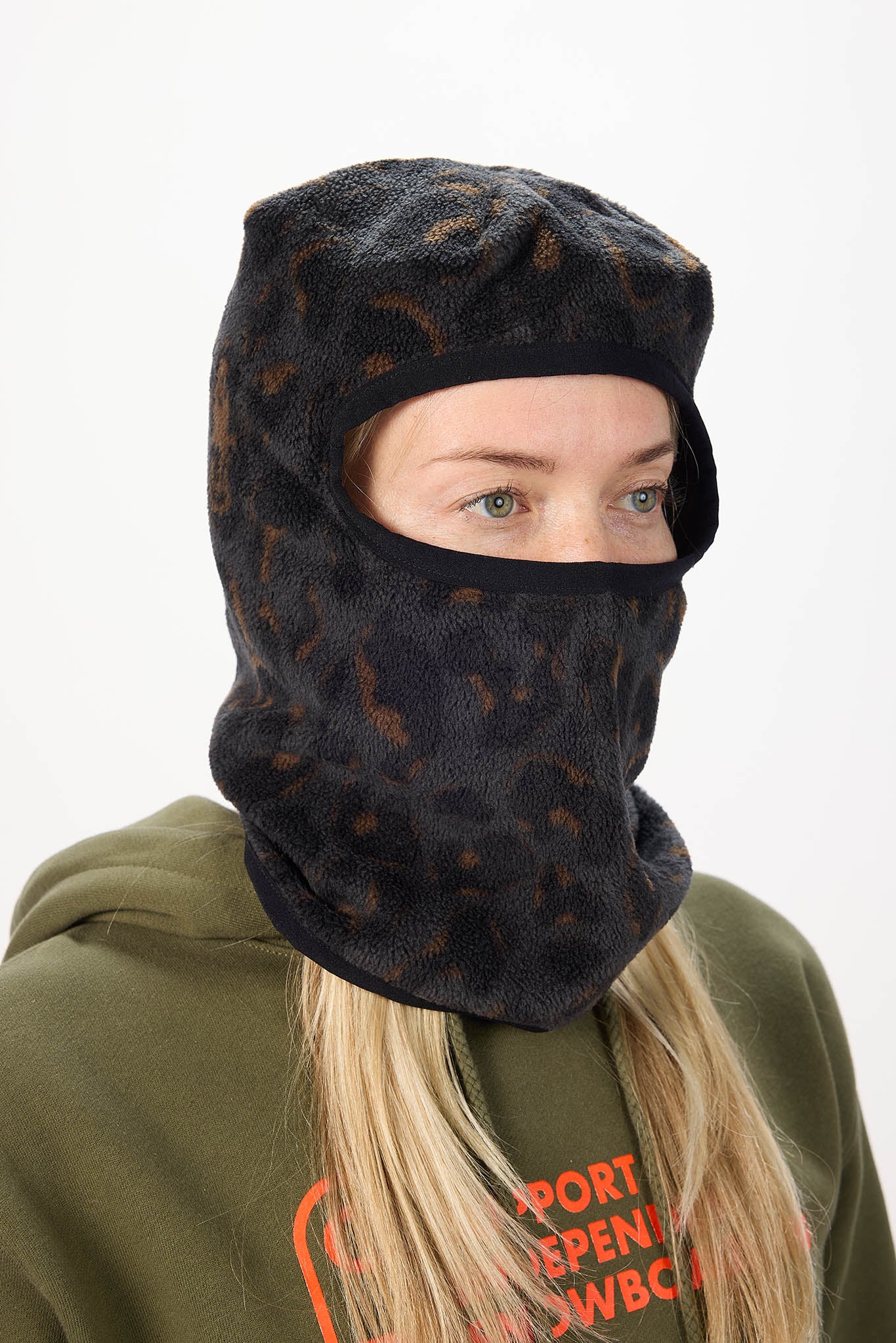 A woman wearing a black fleece balaclava mask with a brown leopard print pattern, paired with an olive green hoodie against a plain white background.