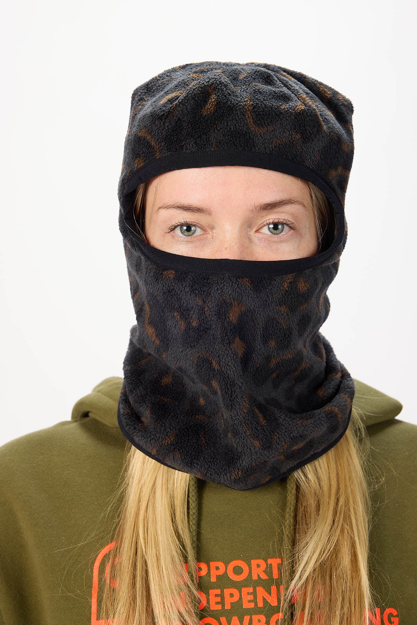 A person wearing a dark leopard print balaclava-style face covering with a subtle brown abstract pattern, paired with an olive green hoodie against a plain light background.