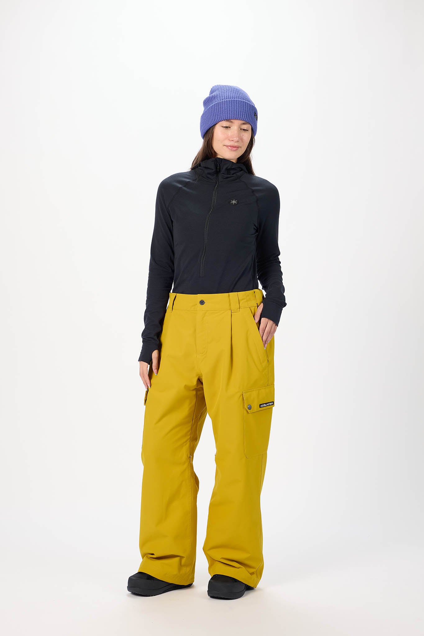 Person wearing a black jacket and yellow pants with a blue beanie on a white background