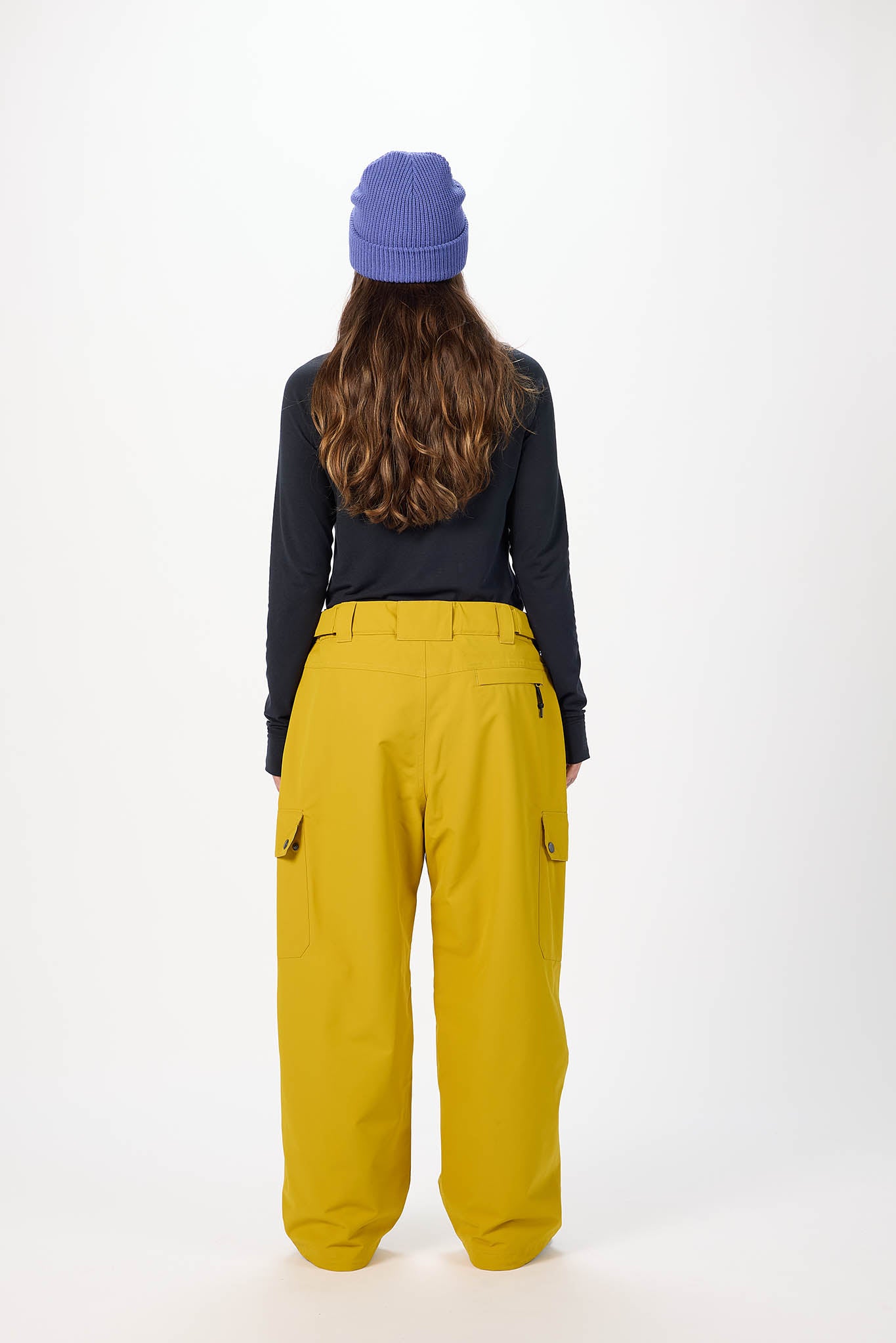 Person wearing mustard yellow pants and a dark long-sleeve top with a white background