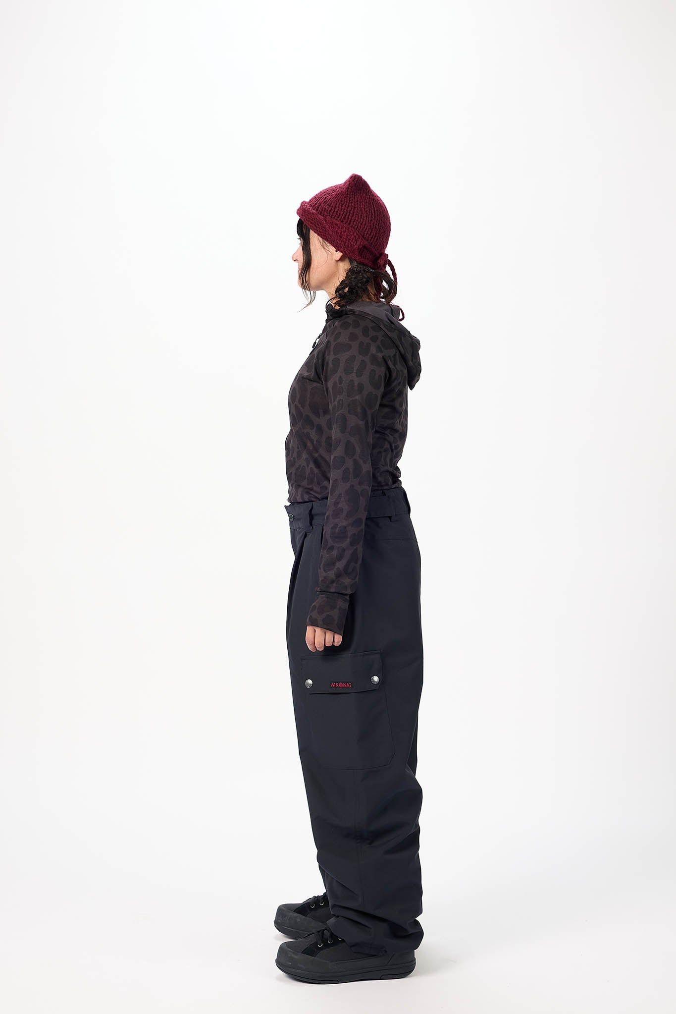 Person wearing a dark patterned jacket and black pants with a red beanie on a white background