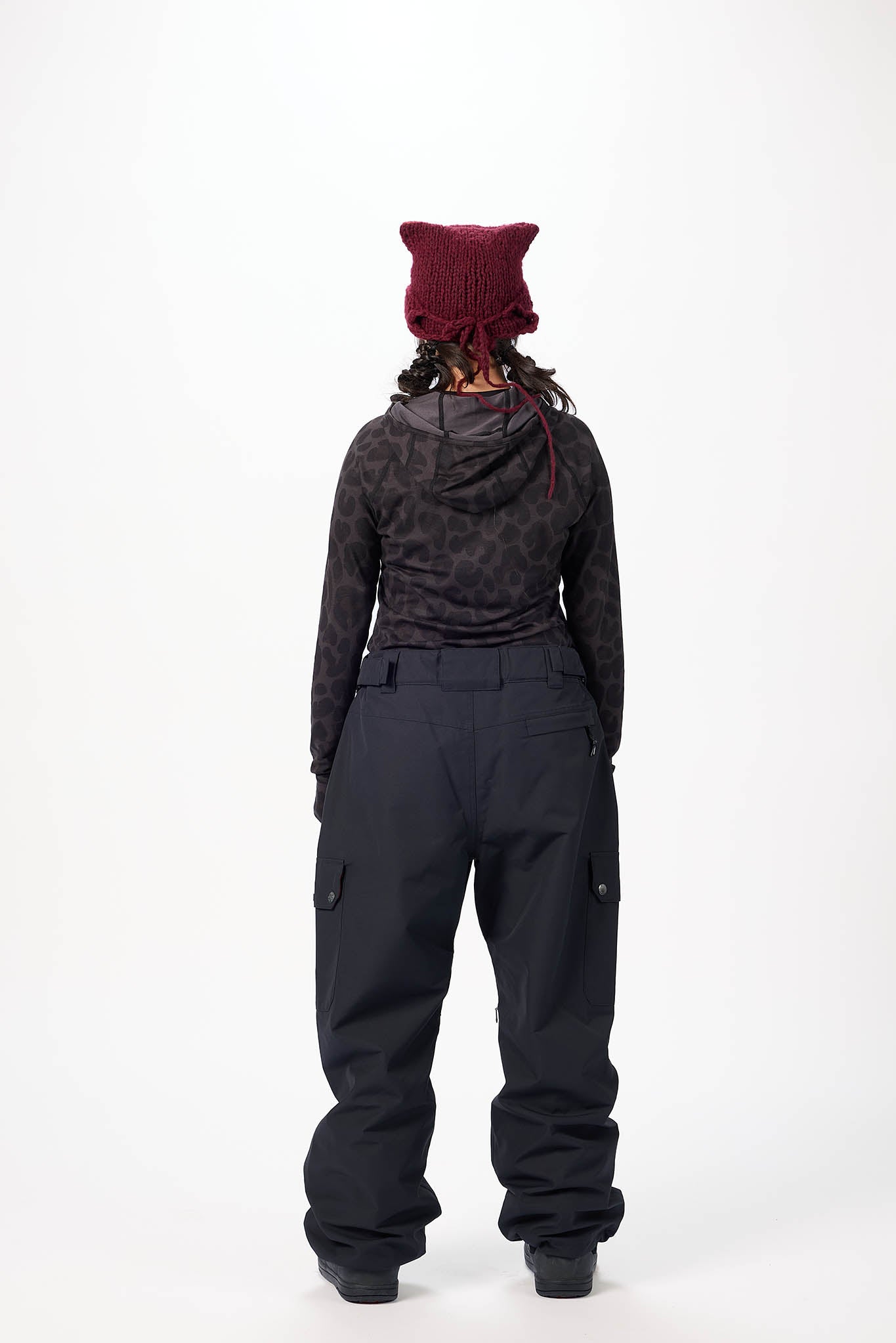 Person wearing a dark jacket and black pants with a red beanie on a white background