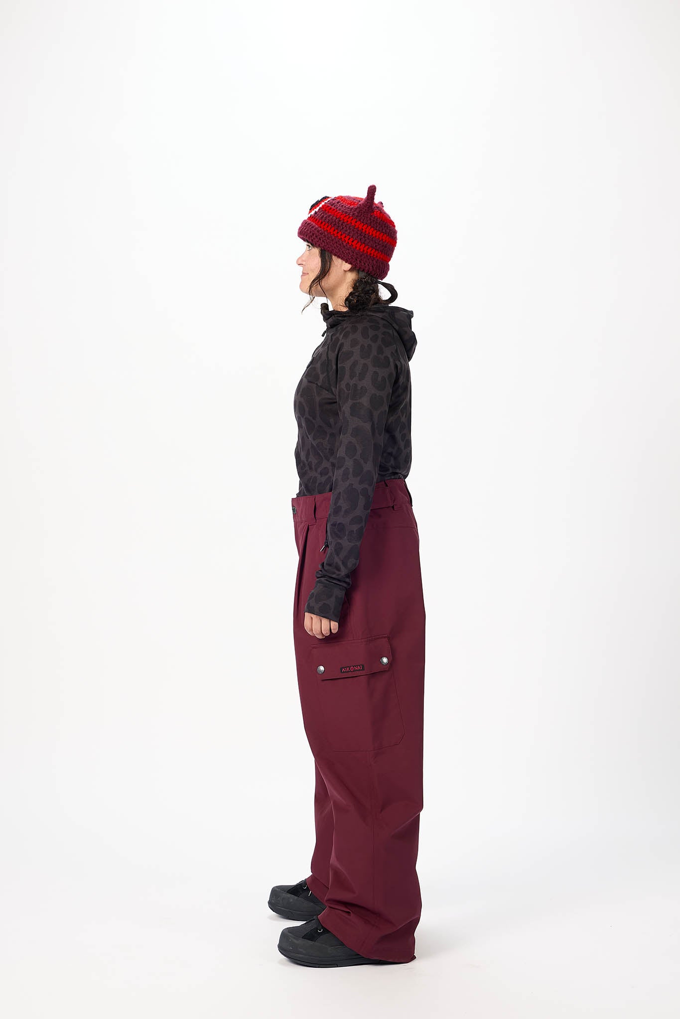 Person wearing a dark patterned jacket, red pants, and a red knit hat on a white background