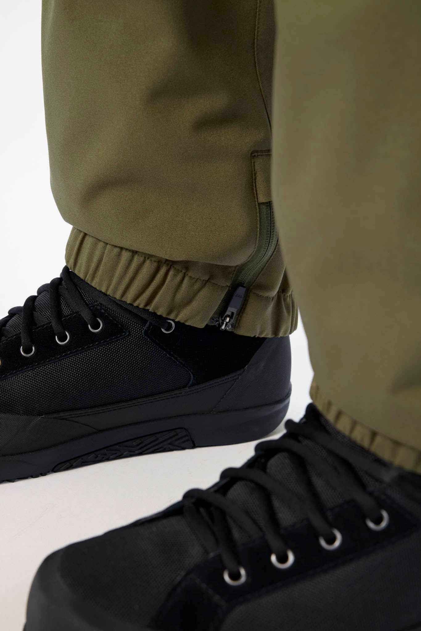 Close-up of black shoes and green pants on a white background