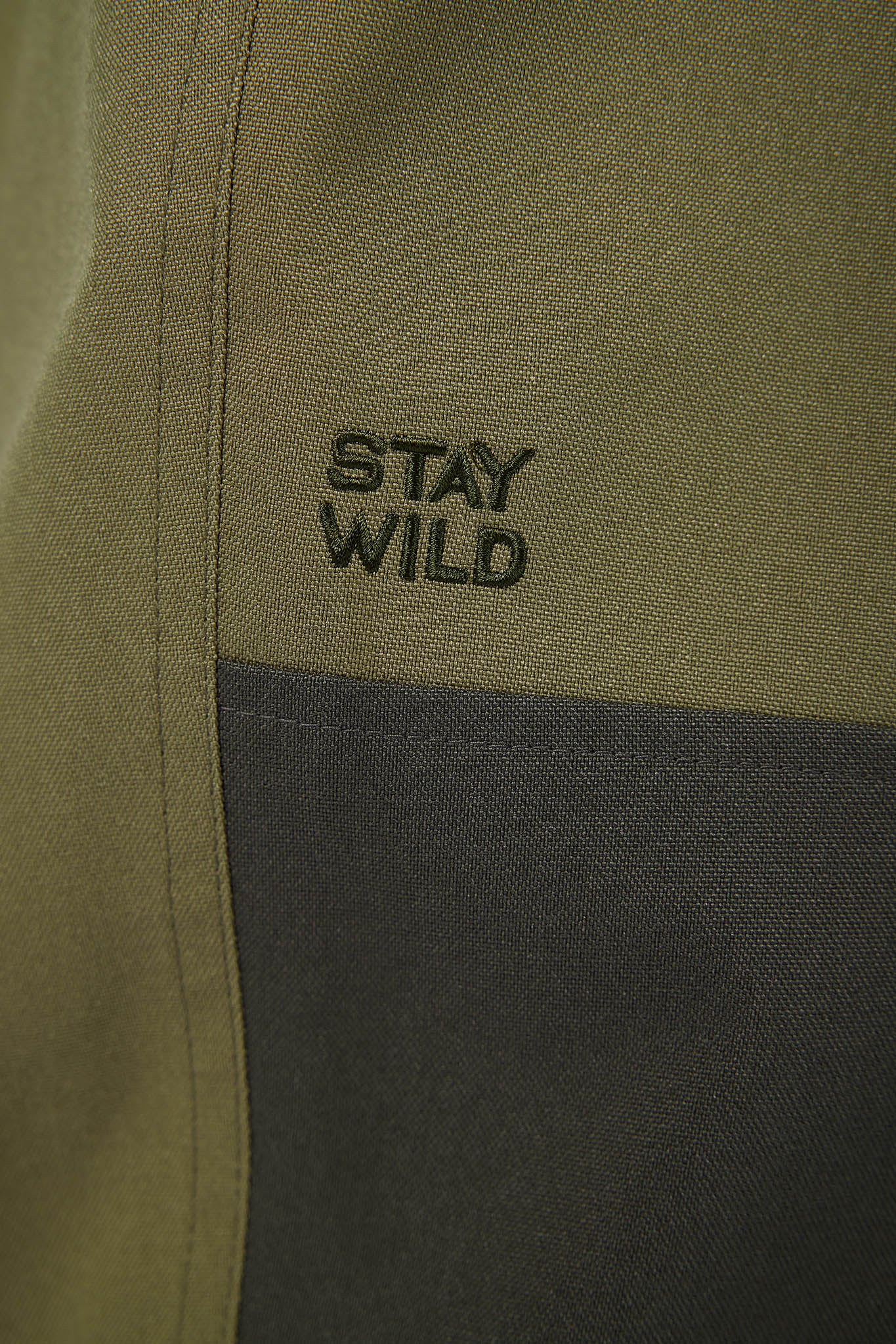 Close-up of a green and gray jacket with a pocket open on a white background stay wild