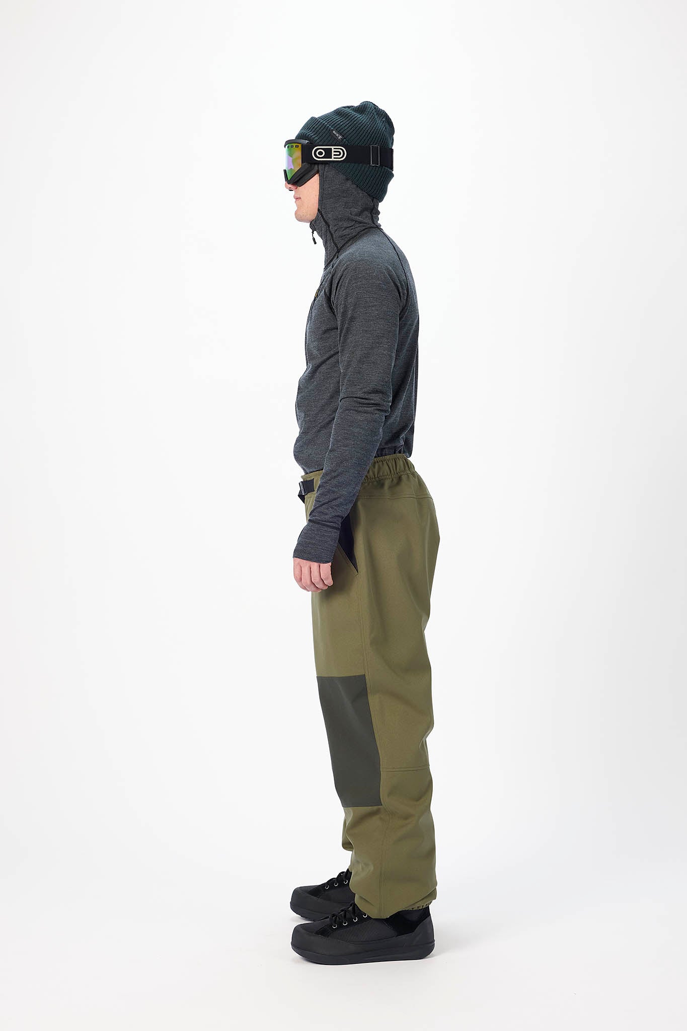 Person wearing a dark gray hoodie, black beanie, and green pants on a white background