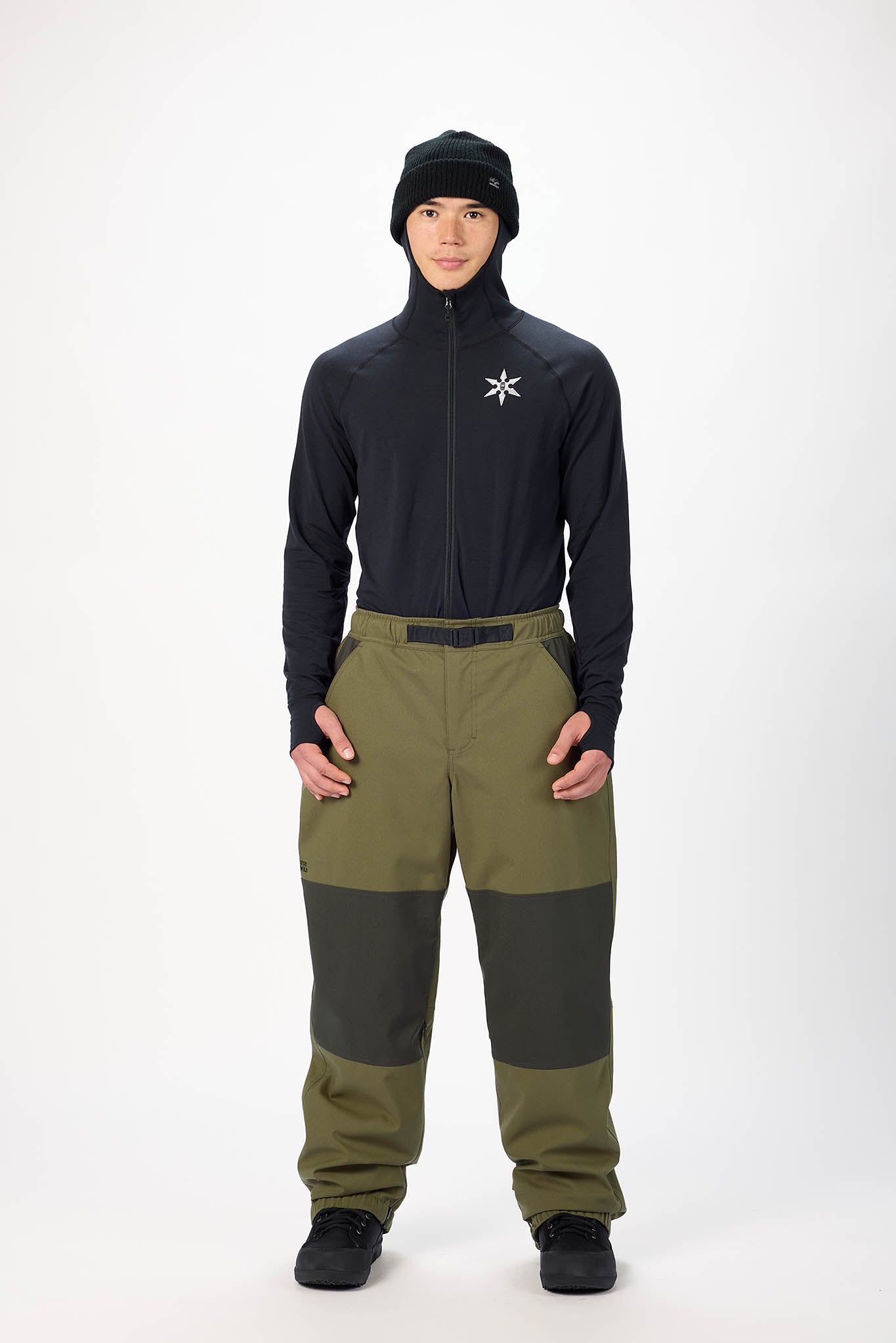 Person wearing a black jacket and green pants on a white background