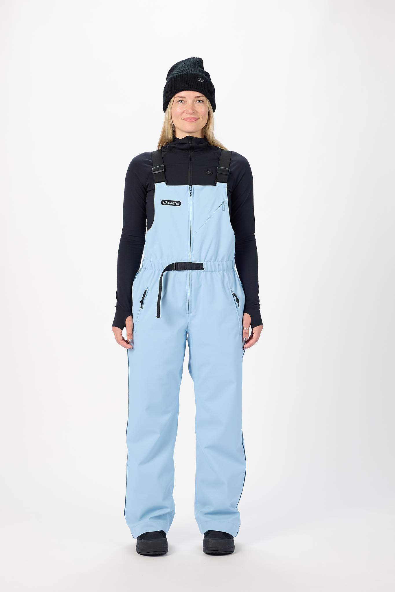 Person wearing light blue bib overalls and black top on a white background