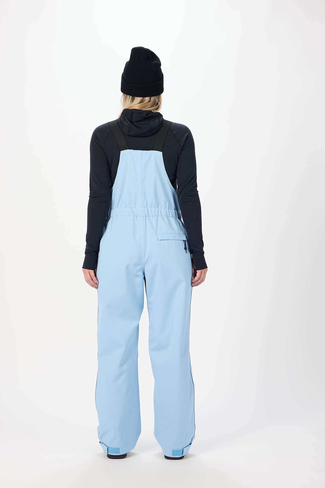 Person wearing a black jacket and light blue bib overalls on a white background