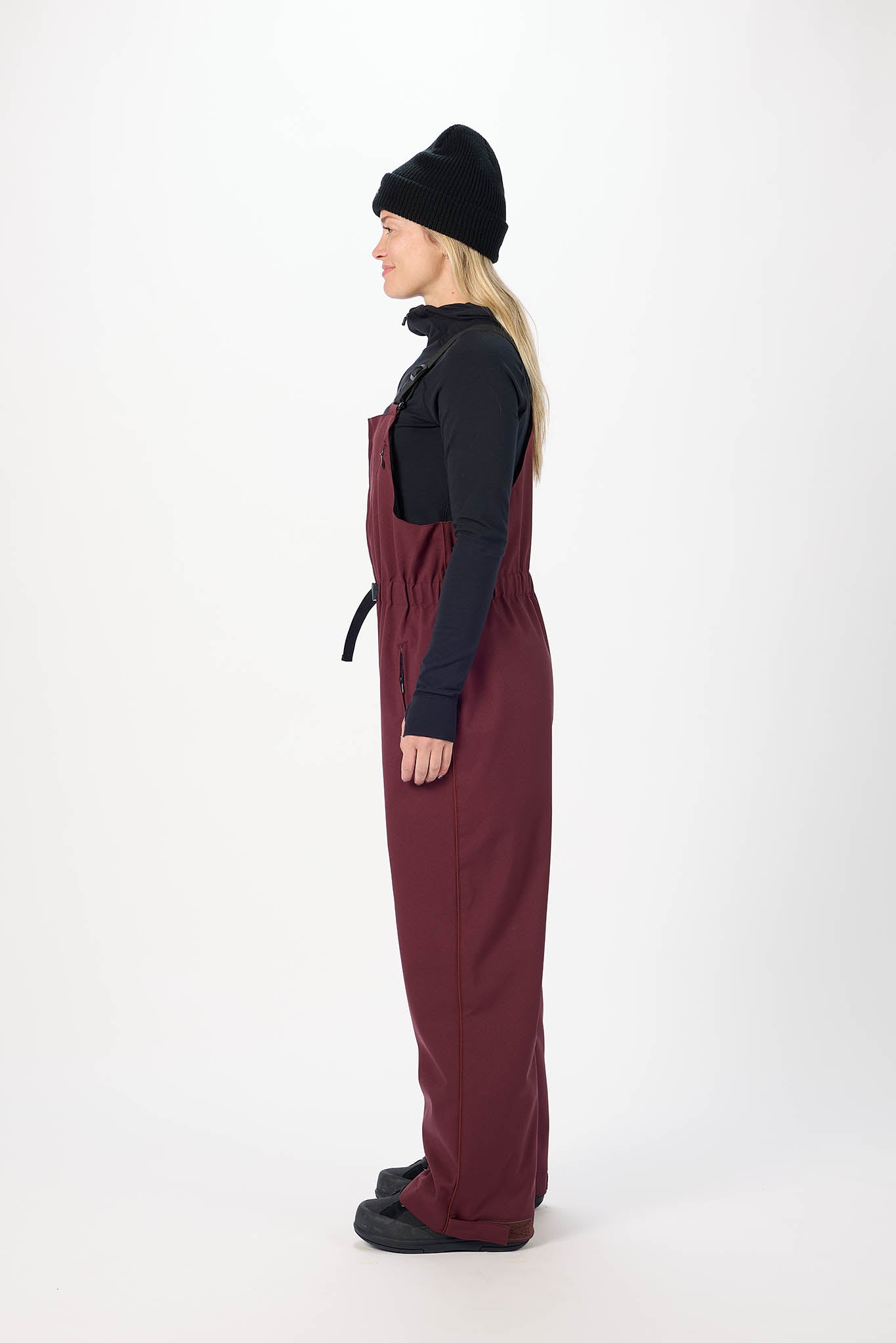 Person wearing a dark jacket and maroon overalls on a white background