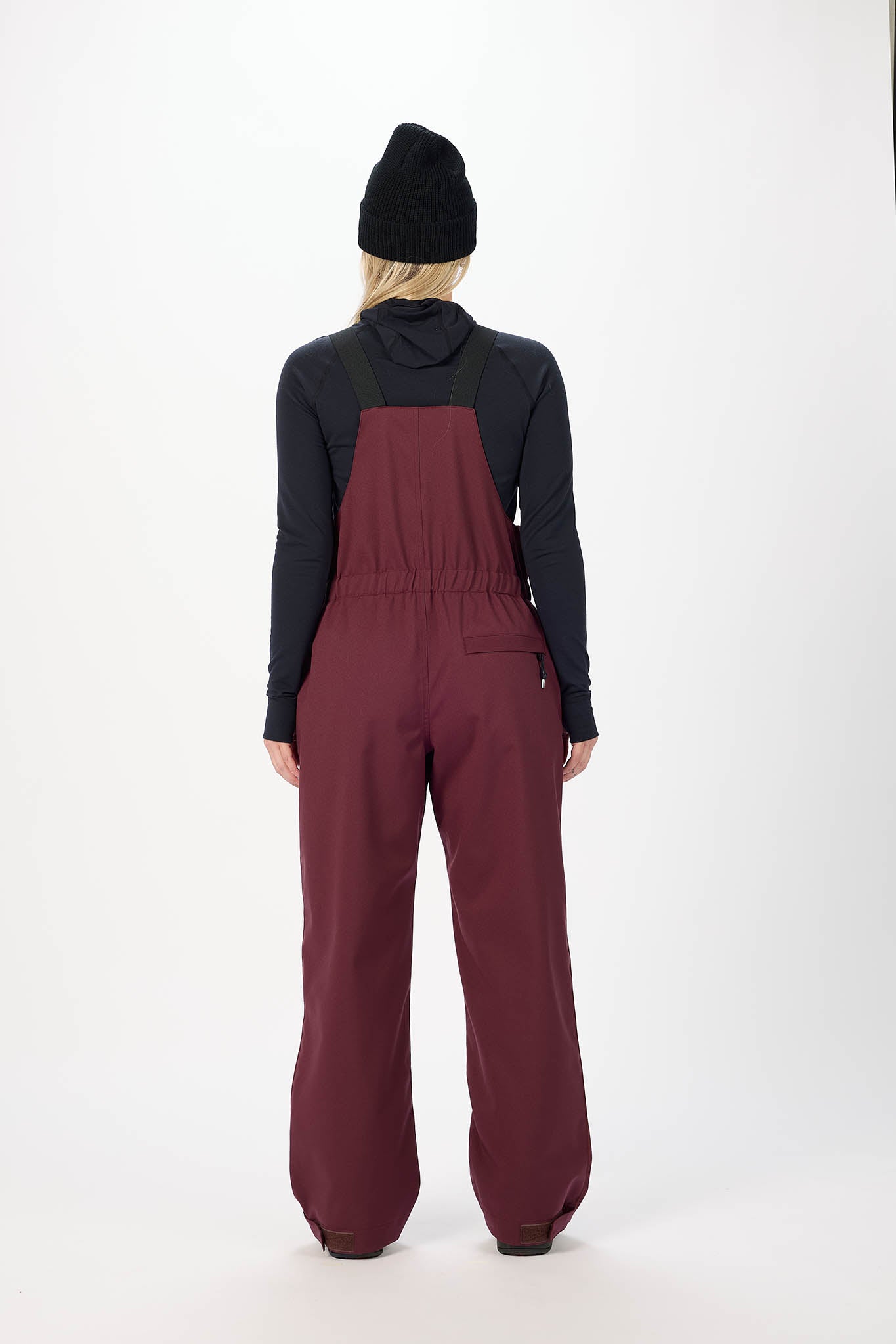 Person wearing a black jacket and maroon overalls on a white background