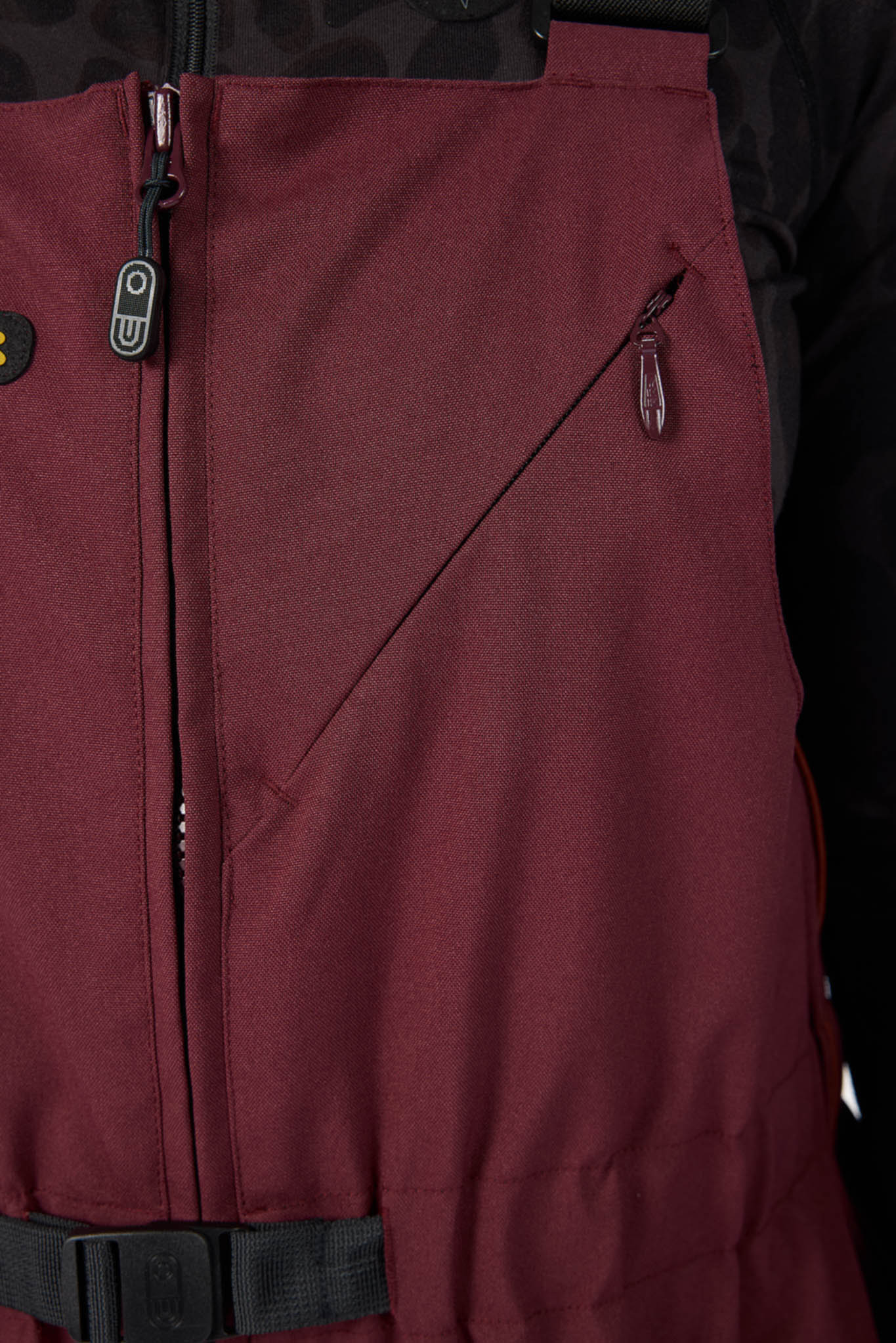 Close-up of a maroon jacket with zippers and buttons on a black background