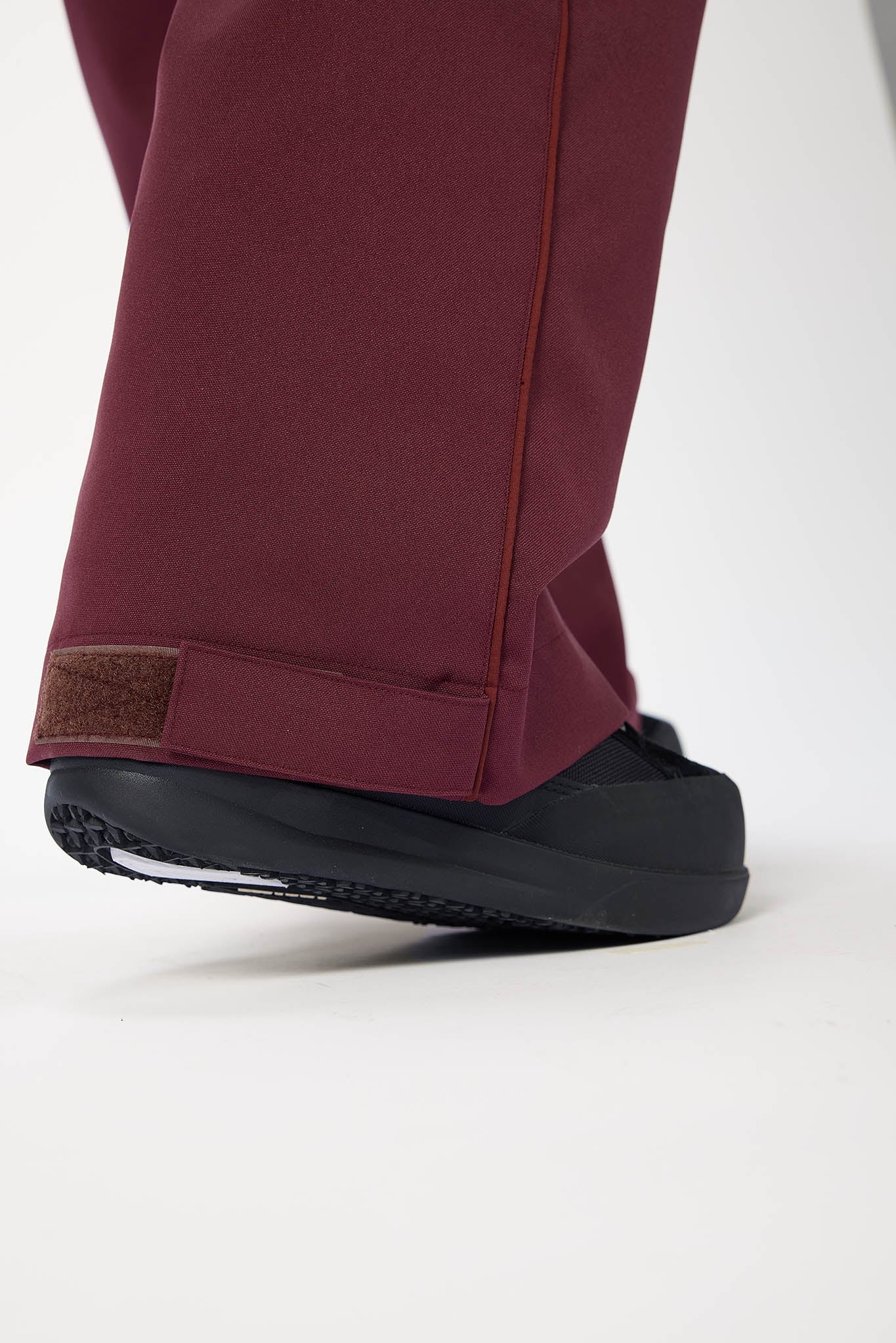 Close-up of maroon pants with a black sole shoe on a white background