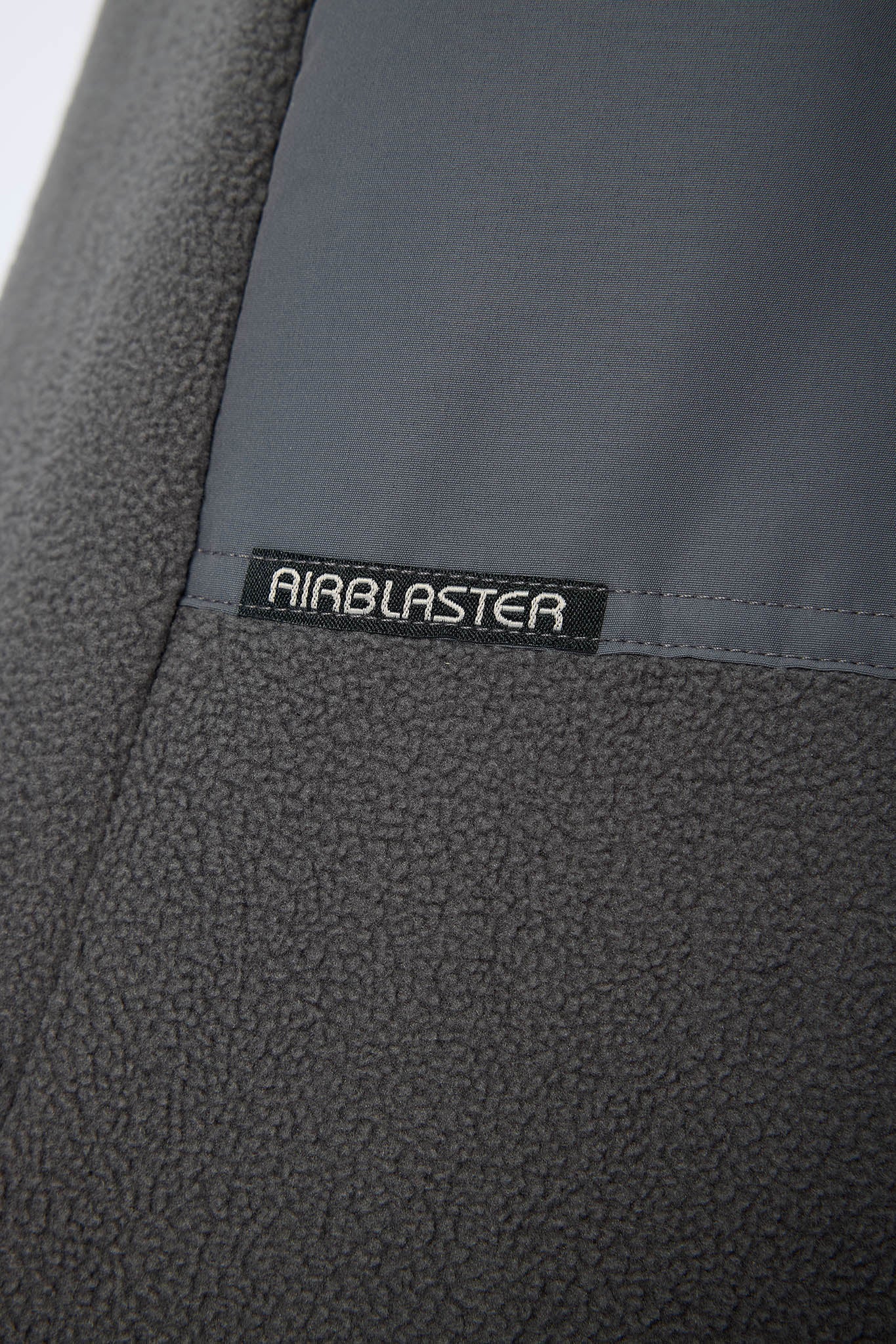 Close-up of a dark gray textured fleece fabric with a smooth gray panel and a black label reading AIRBLASTER.