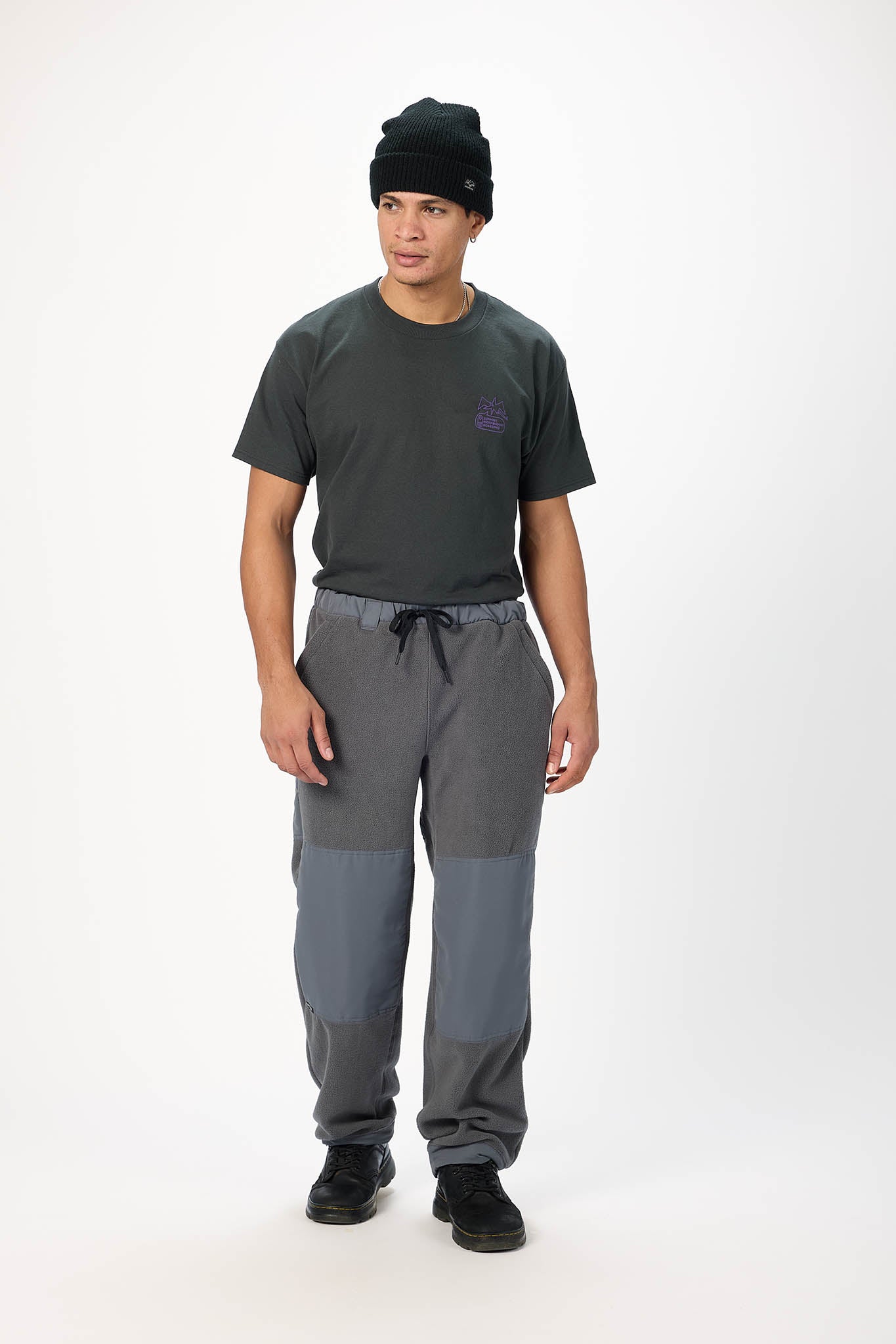 A man modeling a dark gray t-shirt, gray and charcoal colorblock sweatpants, and a black knit beanie against a plain white studio background.