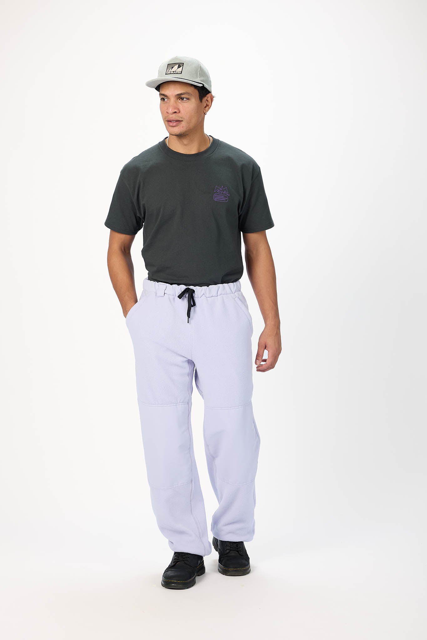 A man modeling a dark charcoal gray t-shirt, light lavender drawstring sweatpants, and a gray baseball cap against a plain white studio background.