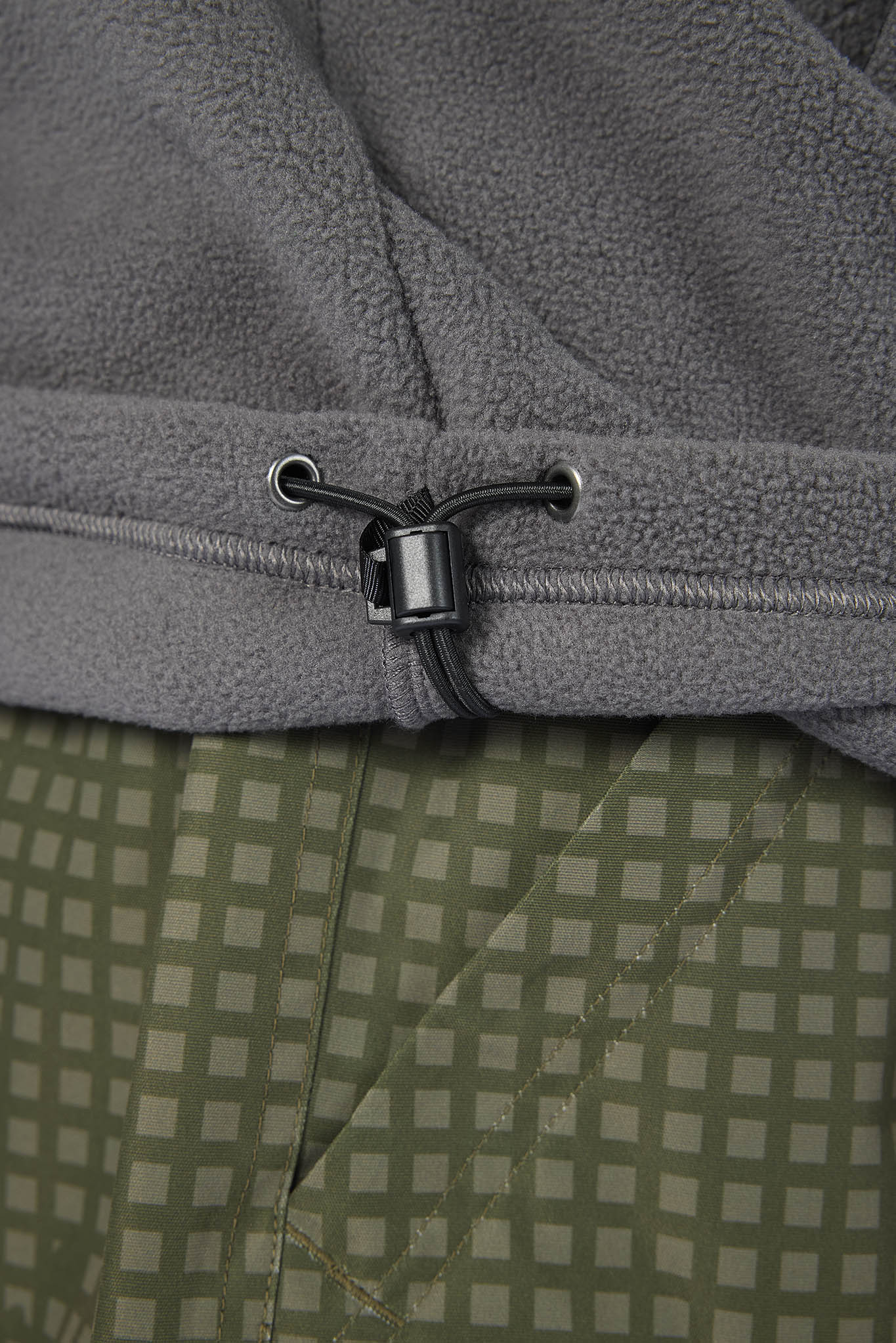 Close-up of a gray fleece garment with a black drawstring toggle, layered over an olive green and beige checkered fabric.