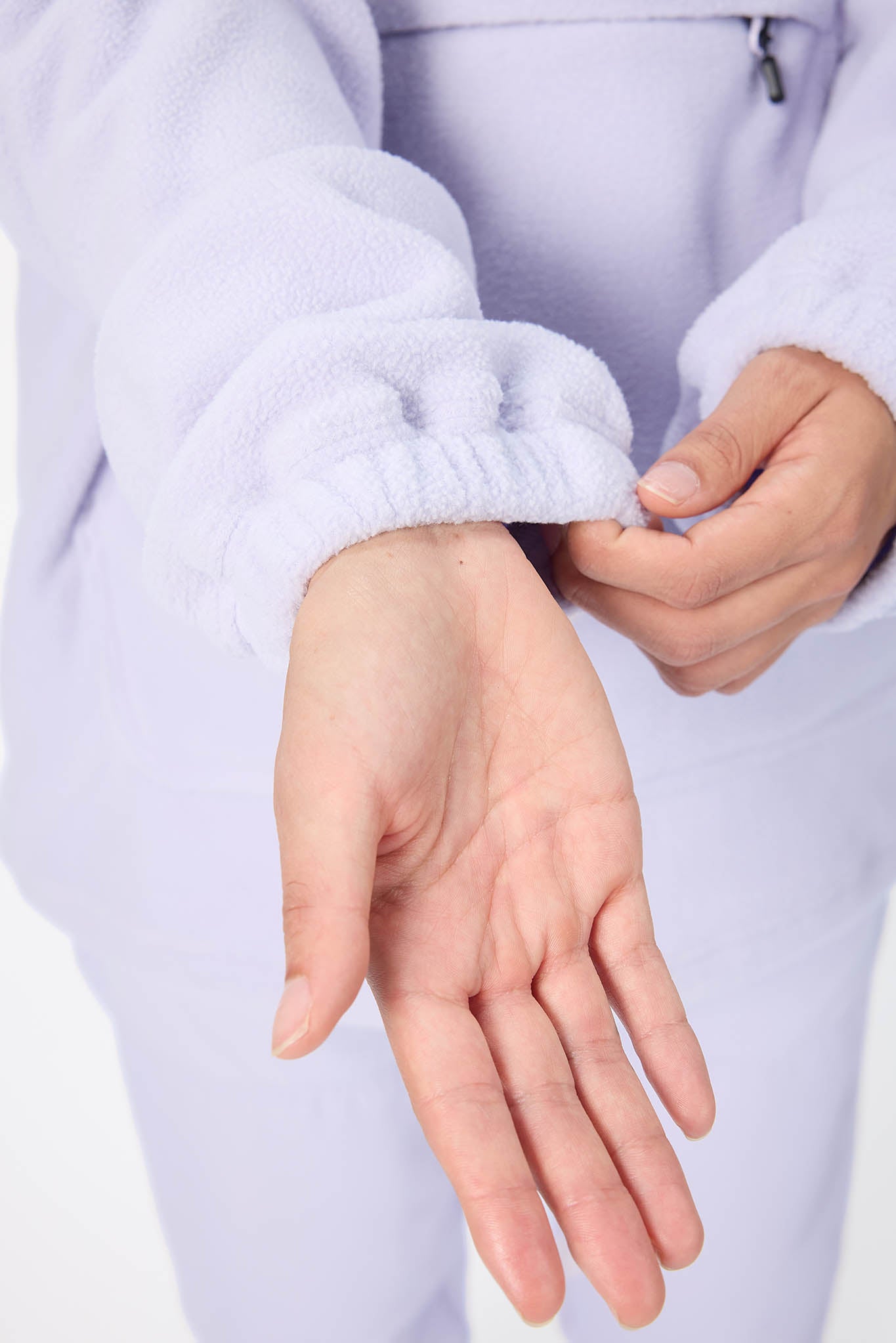 A close-up of a person wearing a light lavender fleece tracksuit, showing the ribbed elastic cuff of the long-sleeve top being adjusted by the hands.