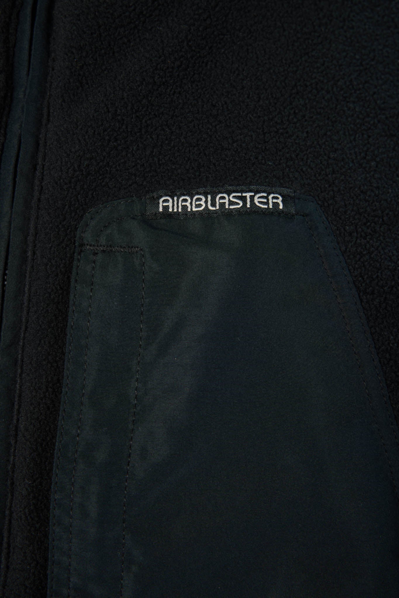 Close-up of a dark navy or black jacket showing a pocket with the word AIRBLASTER embroidered in white on the flap.