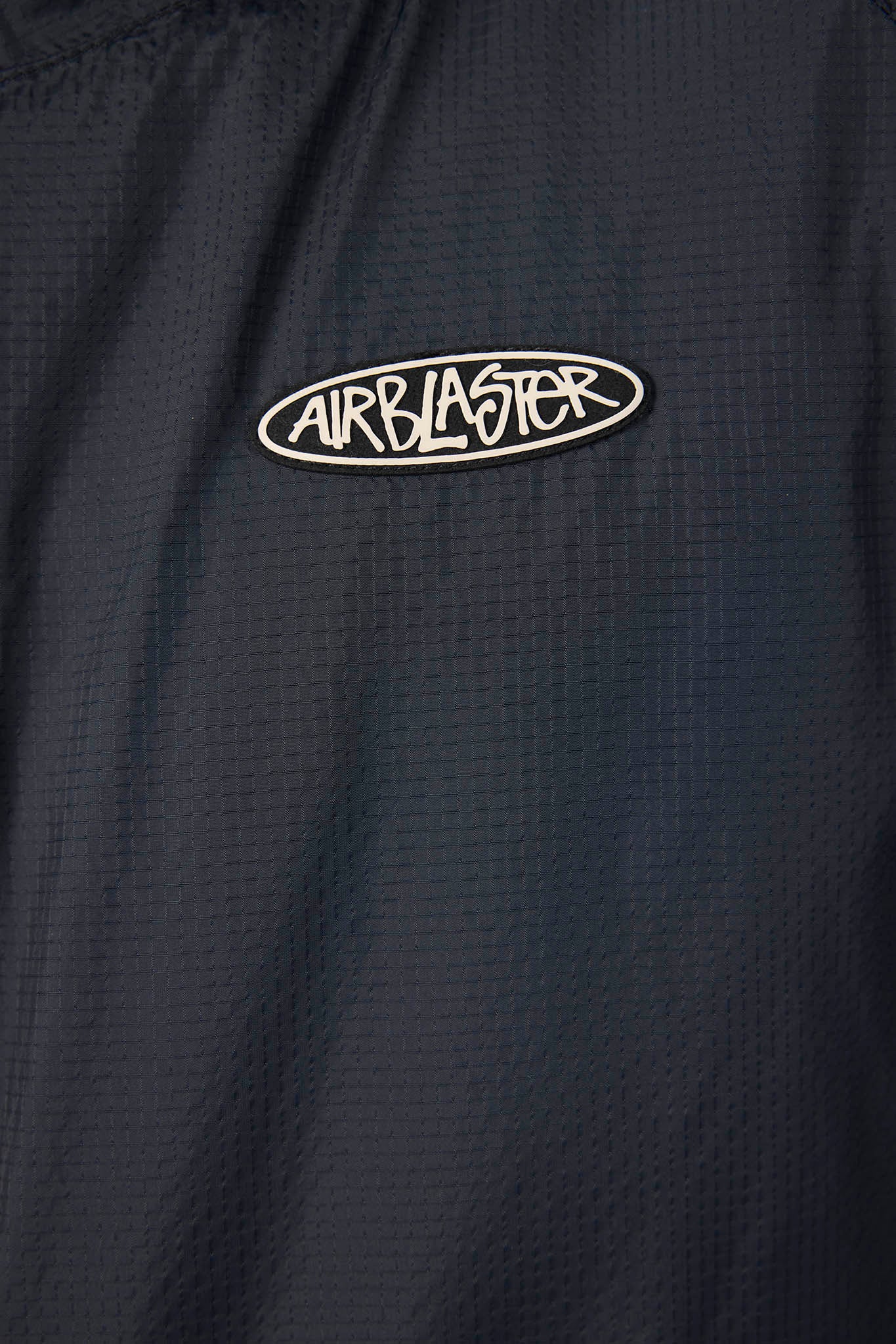 Close-up of a dark navy textured fabric with a white oval Airblaster logo patch on the chest.