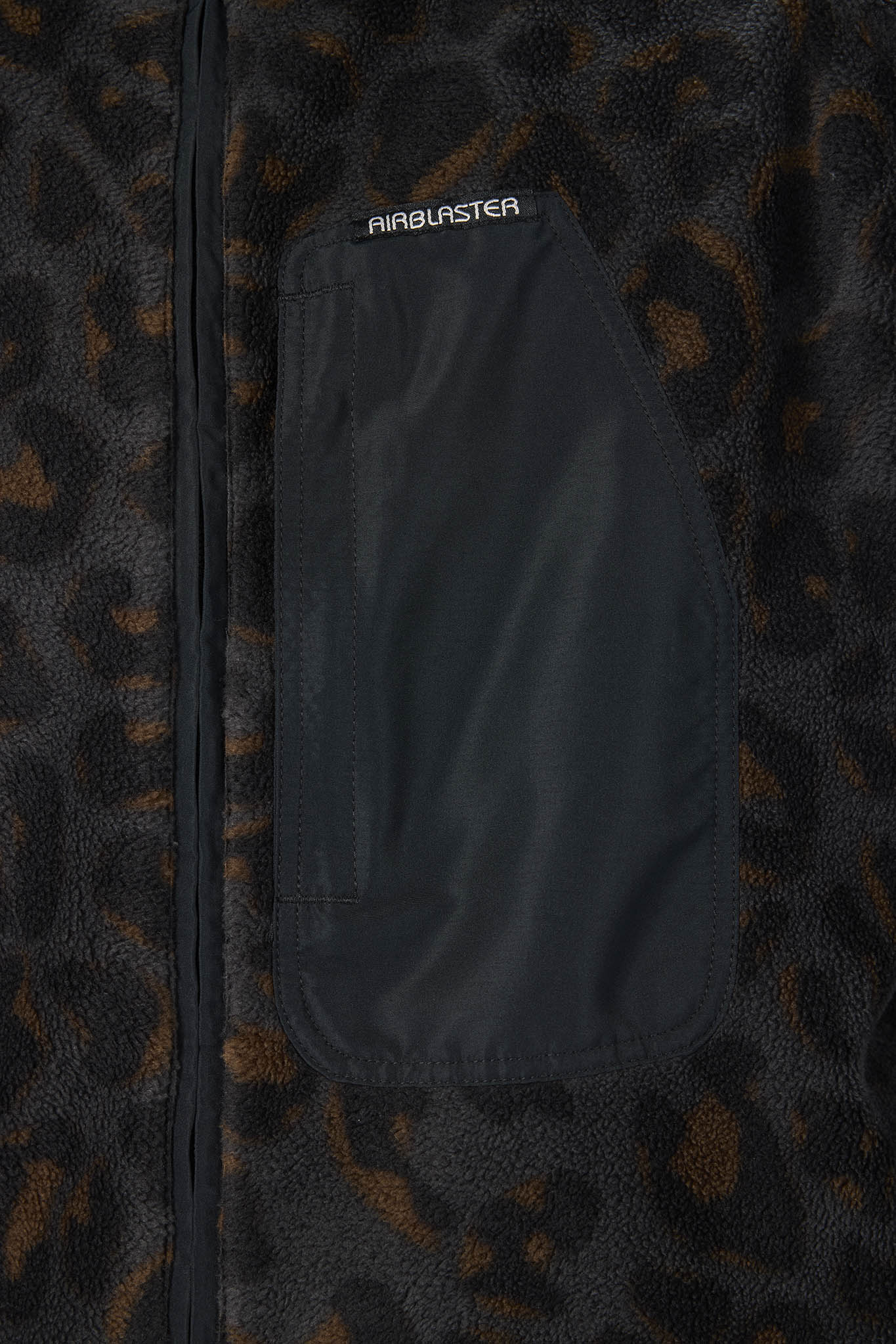 Close-up of a black zip-front jacket with a dark brown and black leopard print fleece body and a large black front pocket. The brand name AIRBLASTER is printed in white on the pocket.