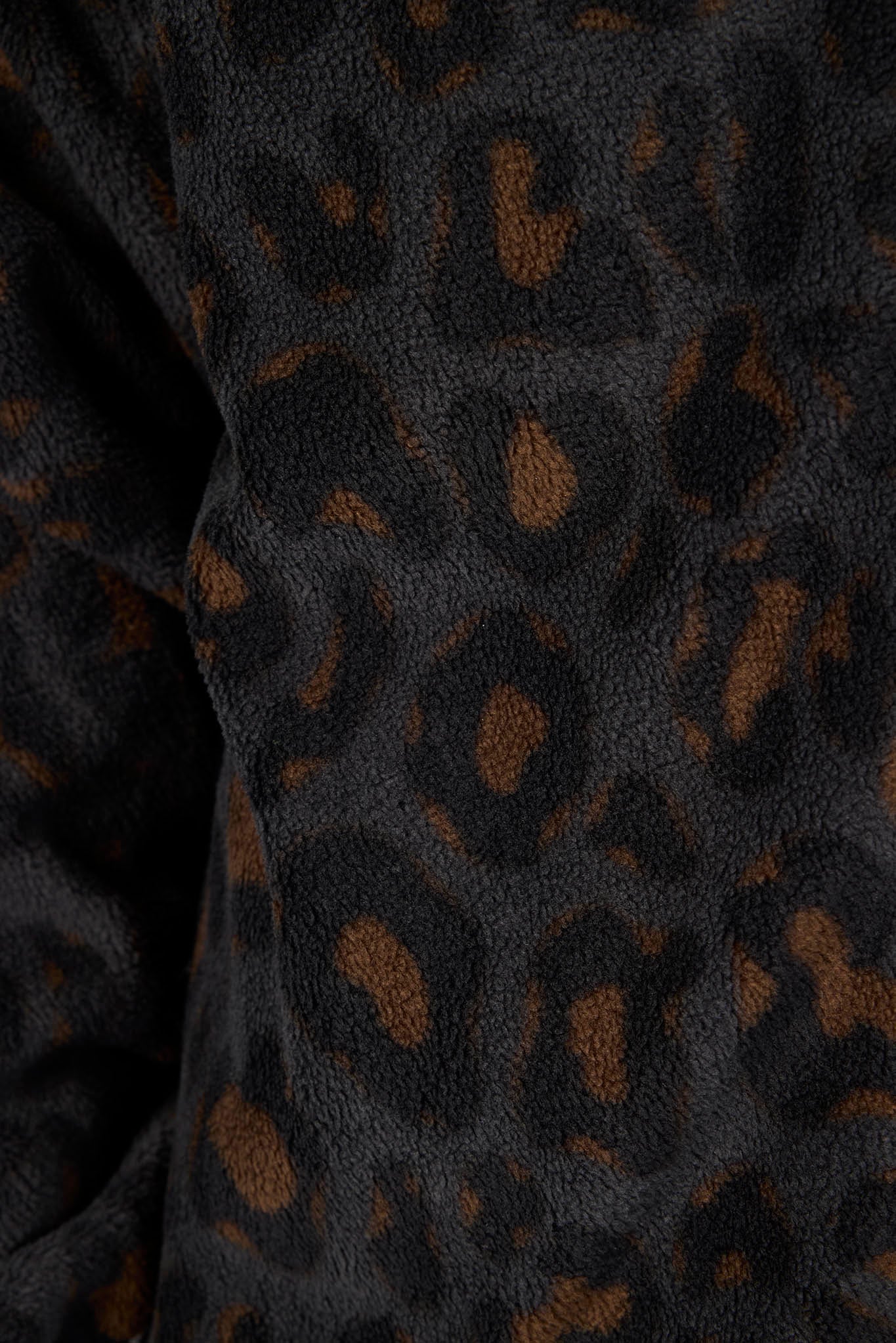 Close-up of a dark leopard print fabric with a soft, textured fleece-like surface.