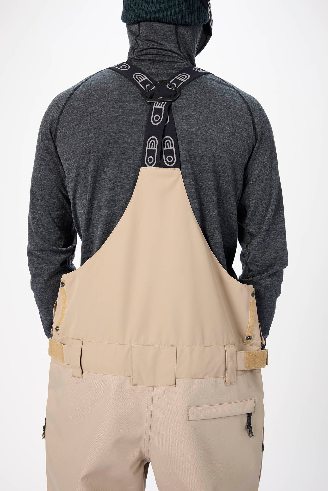 Person wearing beige overalls with a dark gray shirt on a white background