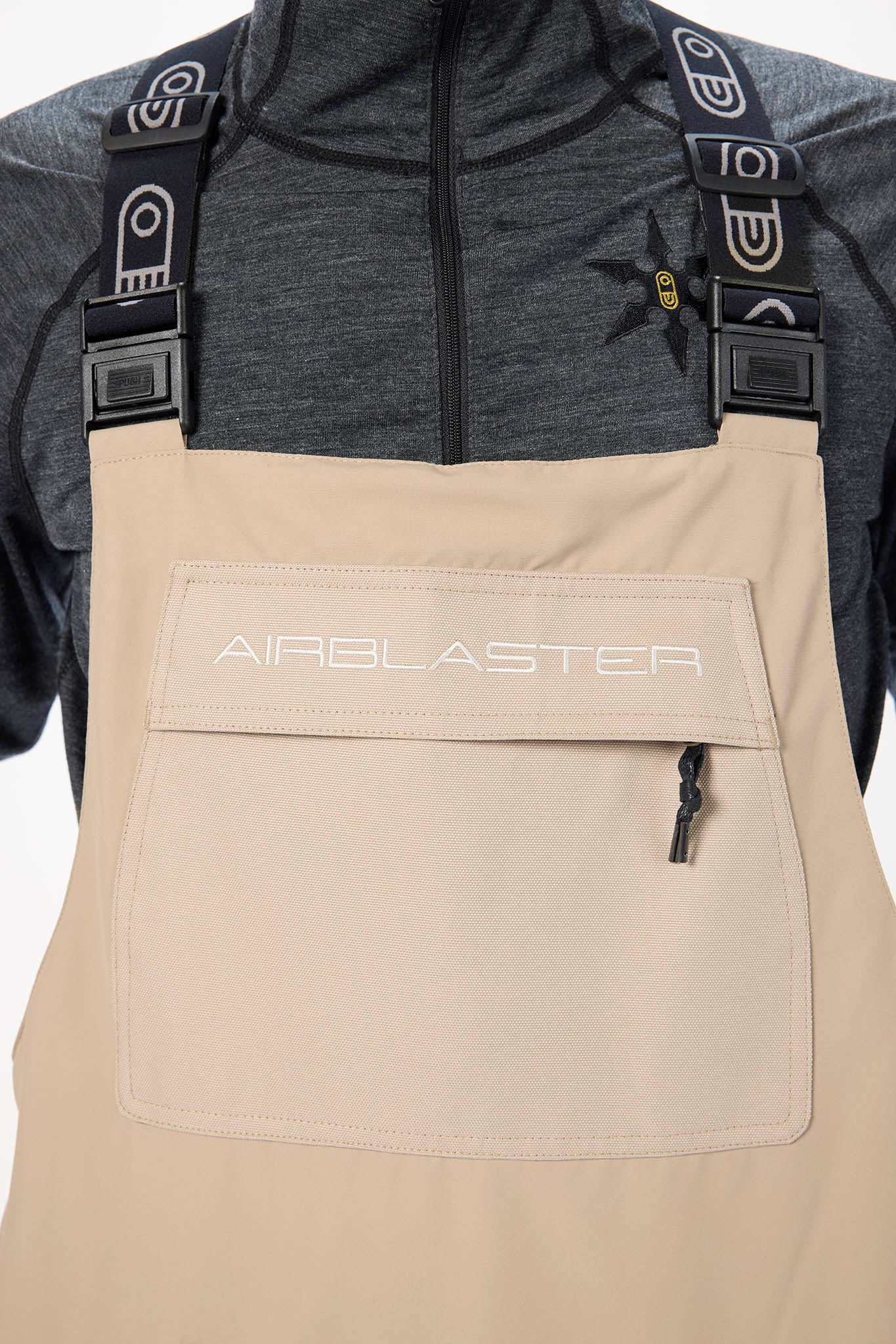 Beige overalls with 'AIRBLASTER' branding worn by a person with a gray shirt underneath.