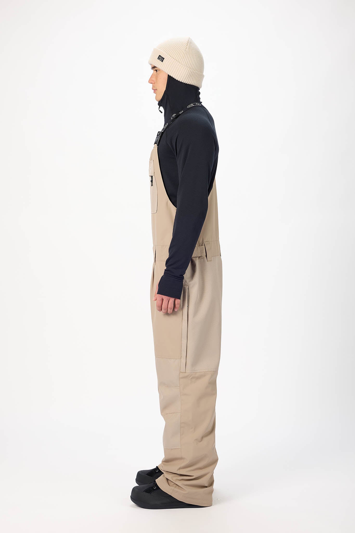 Person wearing a dark jacket, beige pants, and a cream beanie on a white background