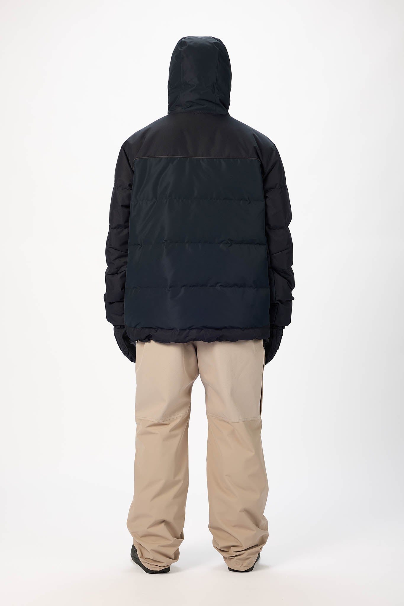 Person wearing a black puffer jacket and beige pants on a white background