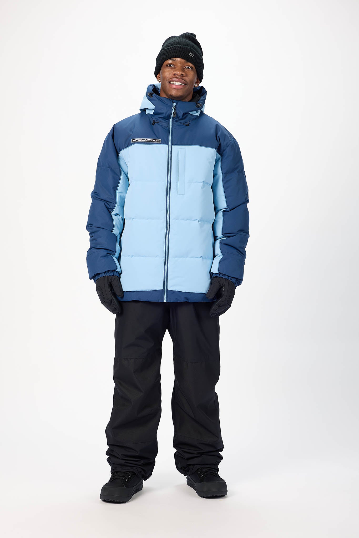 Person wearing a blue and gray winter jacket with black pants on a white background