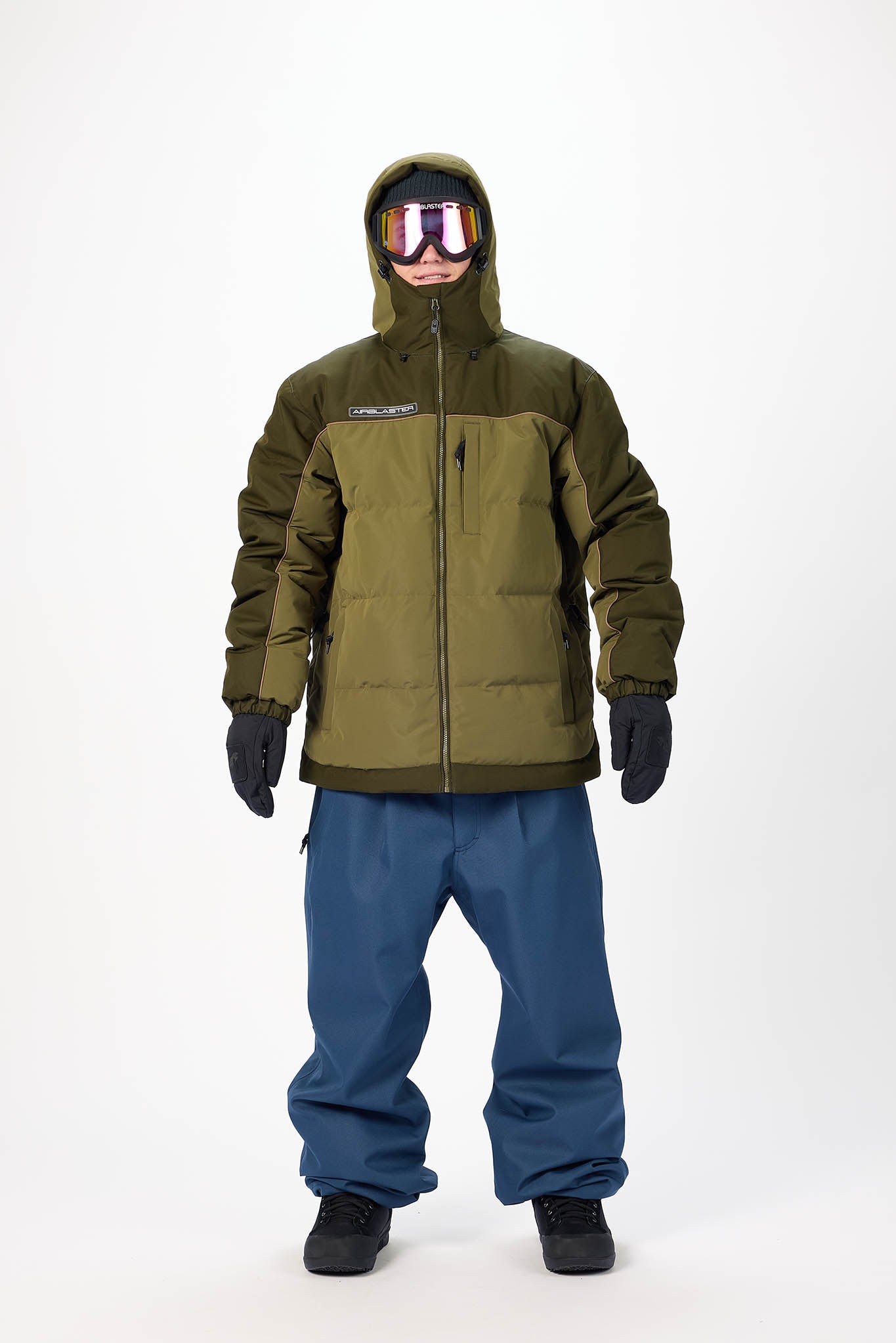 Person wearing a green and blue snowsuit with goggles on a white background