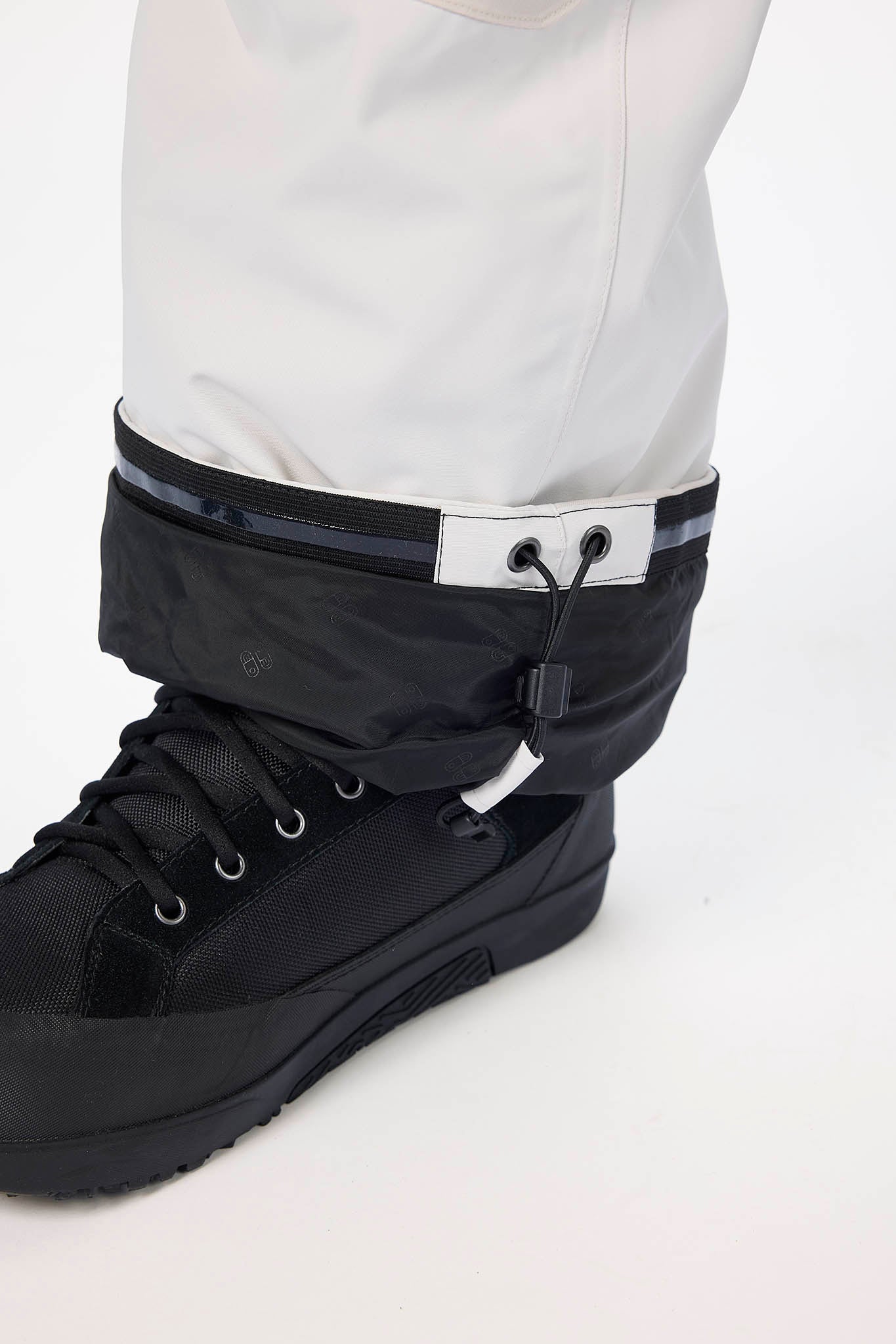 Black boot with gaiters worn over white pants on a white background