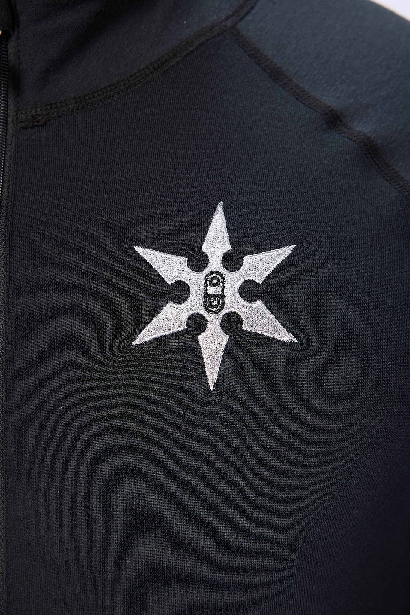 Close-up of a black athletic jacket featuring a silver embroidered six-pointed star logo with a central padlock graphic on the chest.