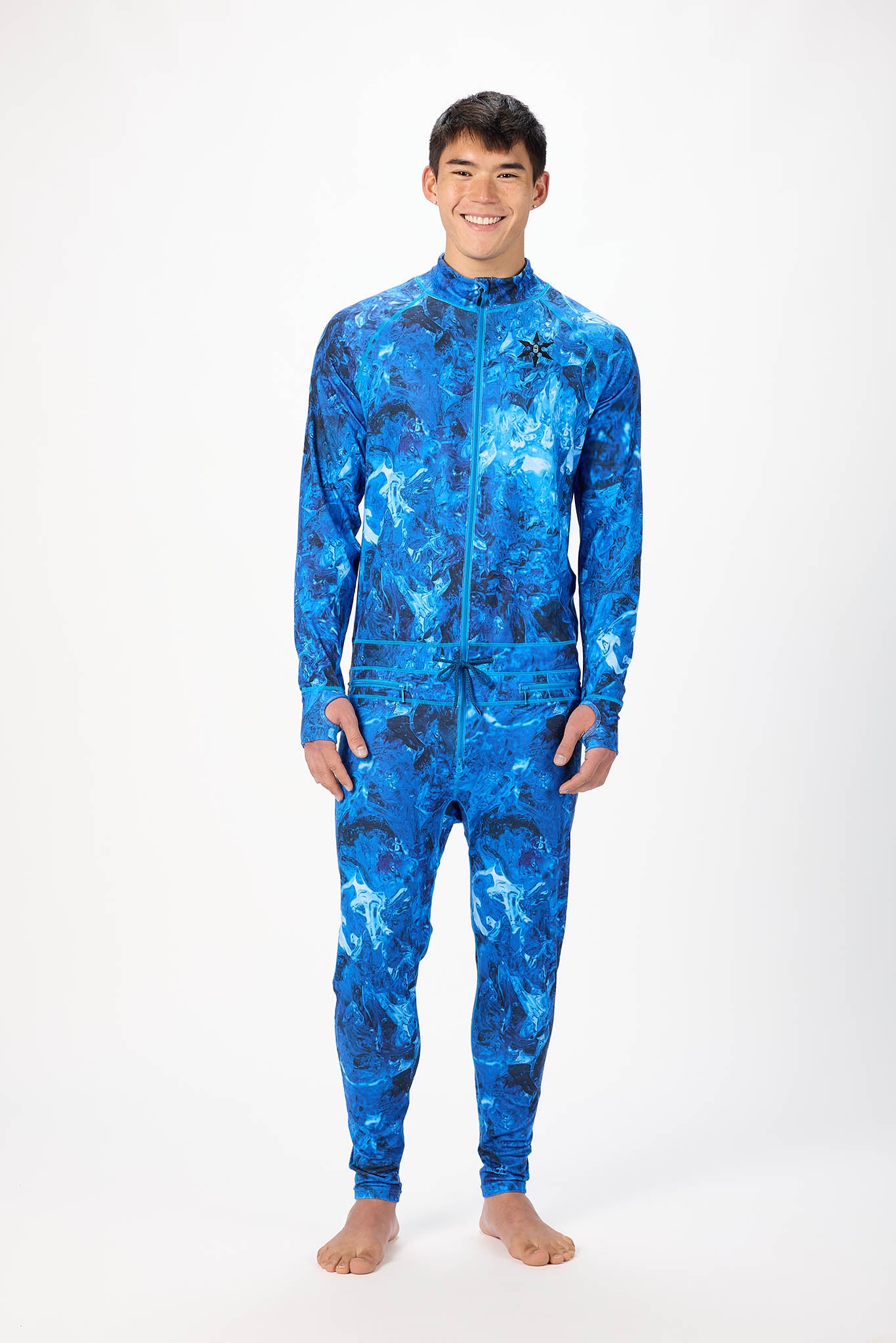 A man modeling a blue abstract pattern full-zip athletic onesie with a small white logo on the left chest, standing against a plain white studio background.