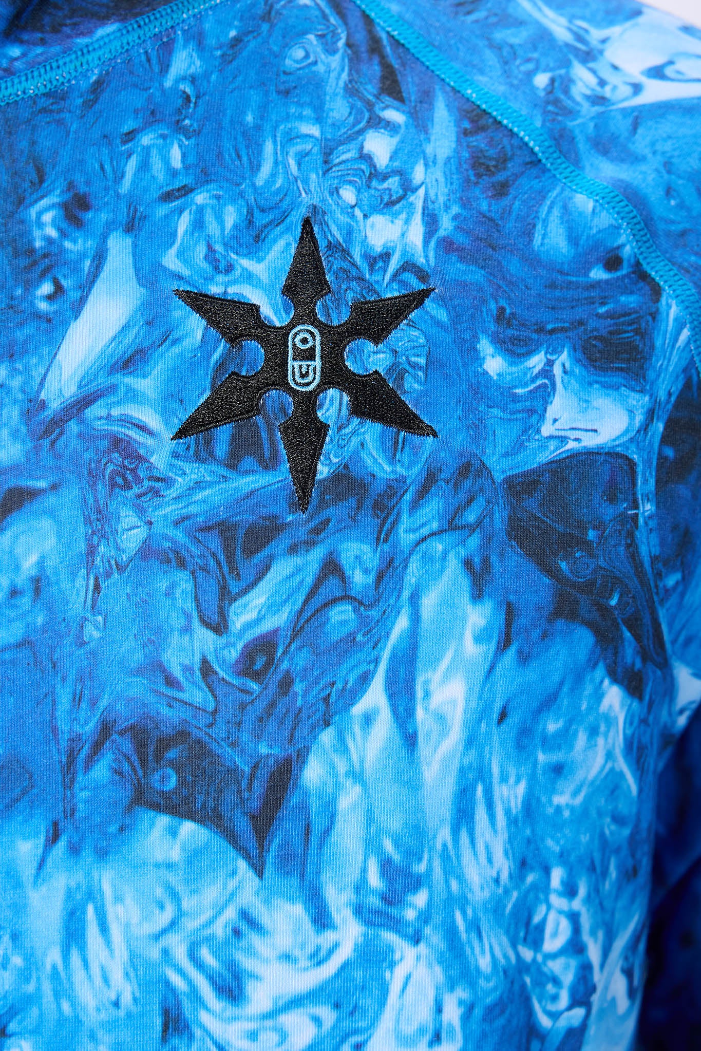 Close-up of a blue patterned garment featuring a black six-pointed star patch with a white circular logo in the center.