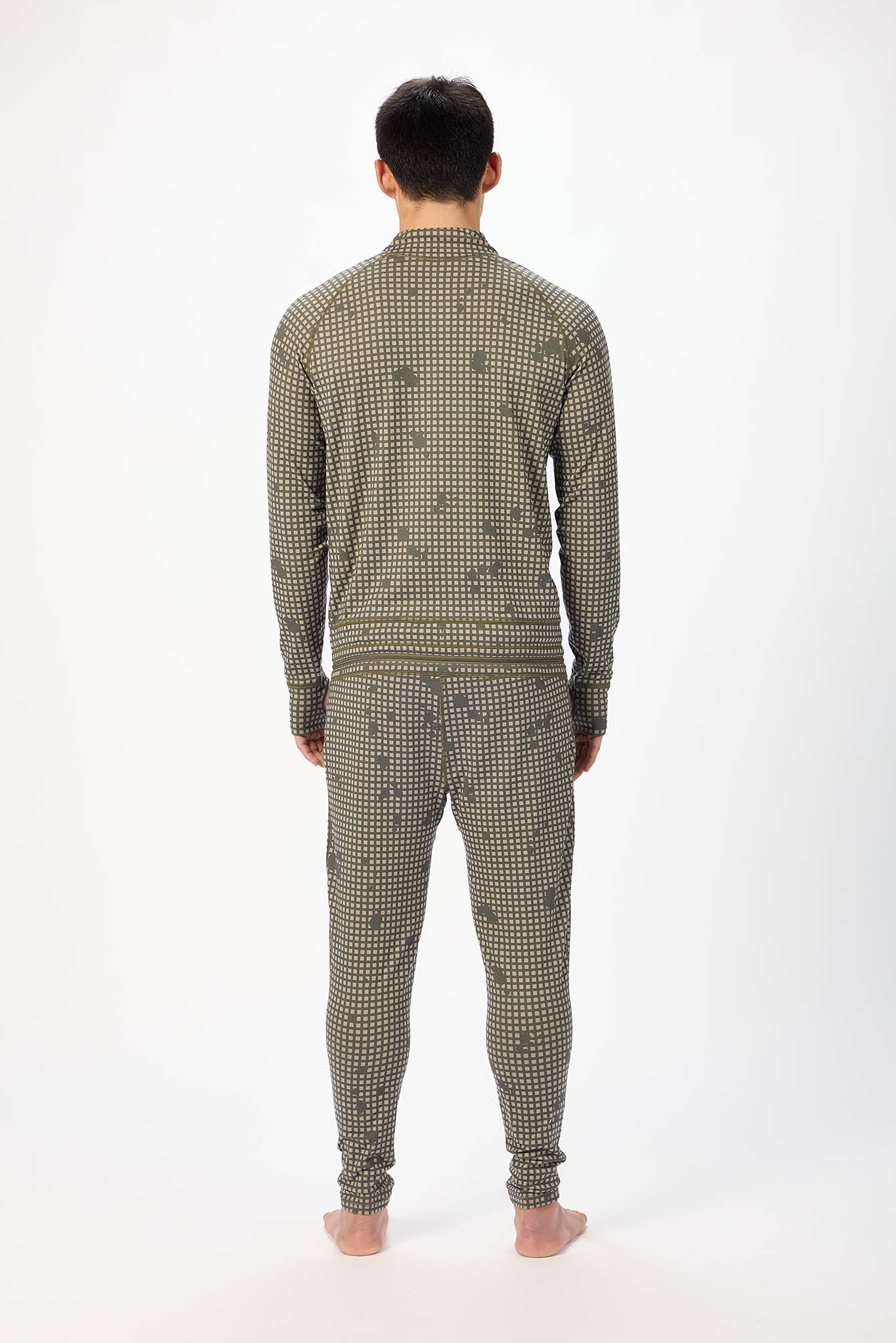 view from behind A man modeling a olive grid like pattern full-zip athletic onesie with a small white logo on the left chest, standing against a plain white studio background.