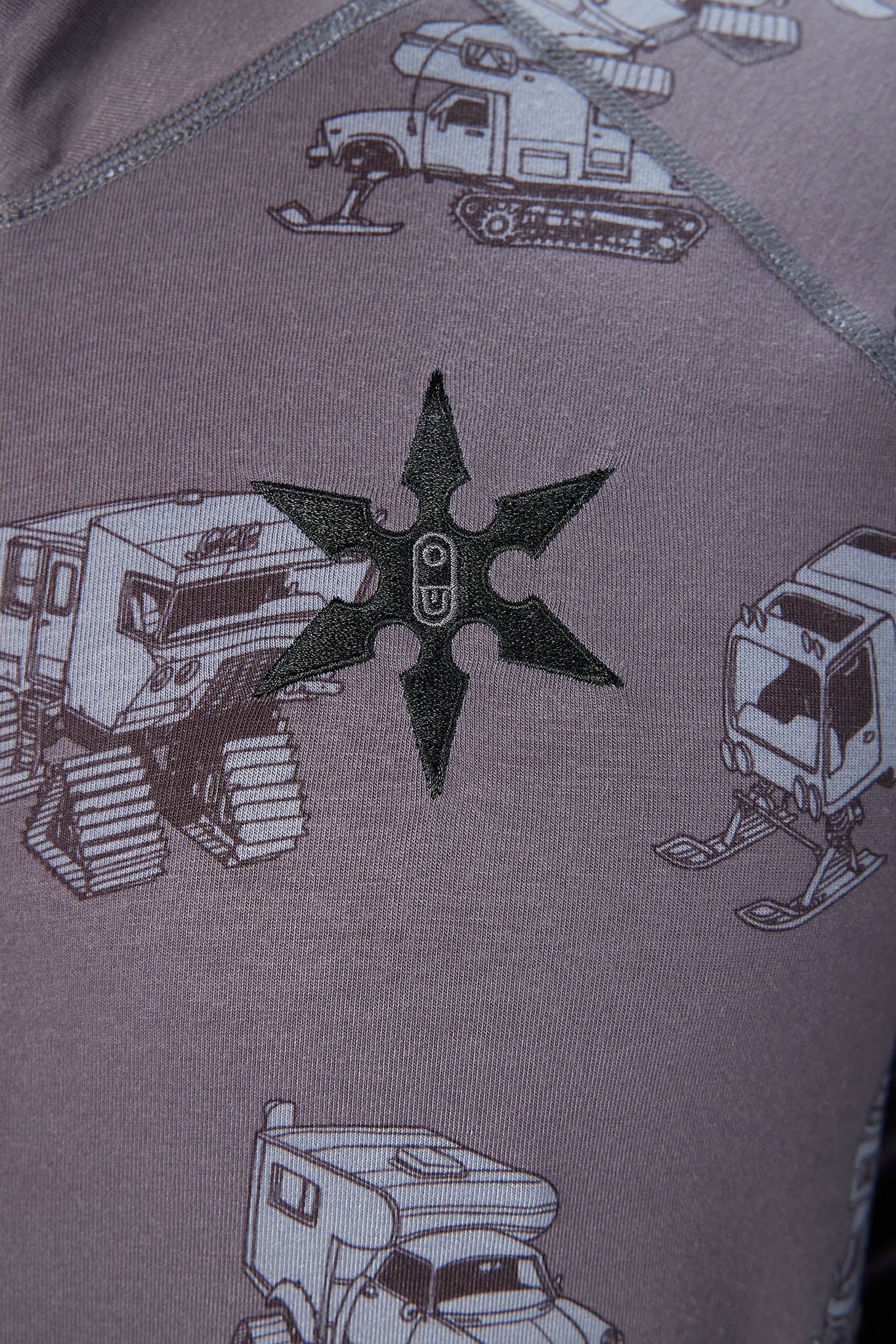 Close-up of a dusty mauve or lavender fabric printed with military-style snow vehicles and a central black star-shaped emblem