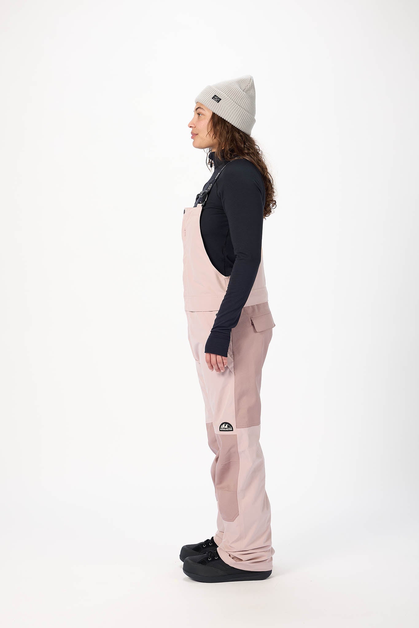 Person wearing a black jacket, pink pants, and a gray beanie on a white background