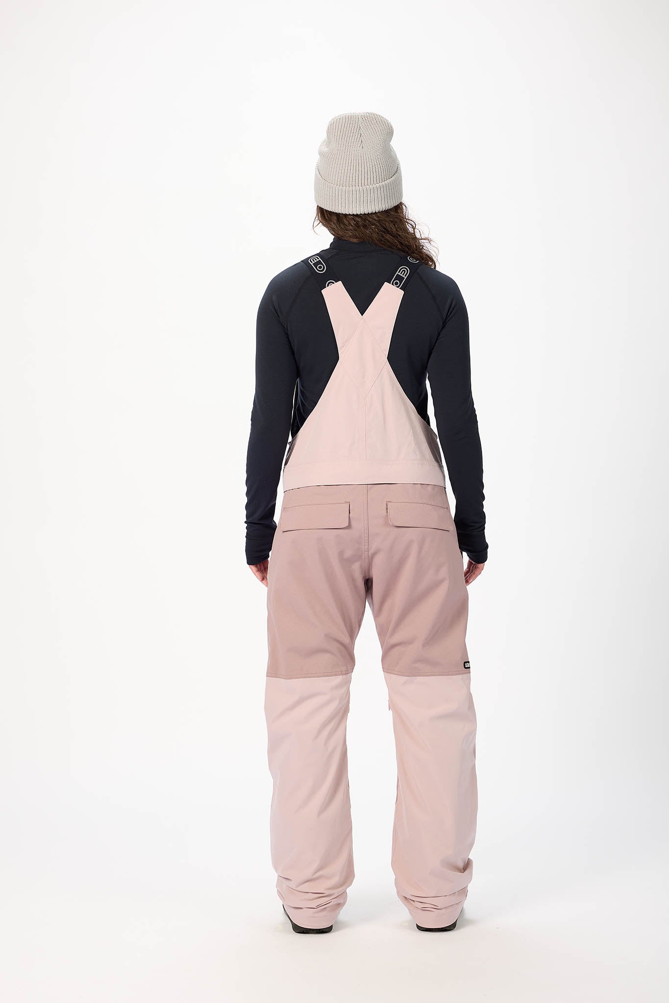 Person wearing a black top and pink overalls on a white background
