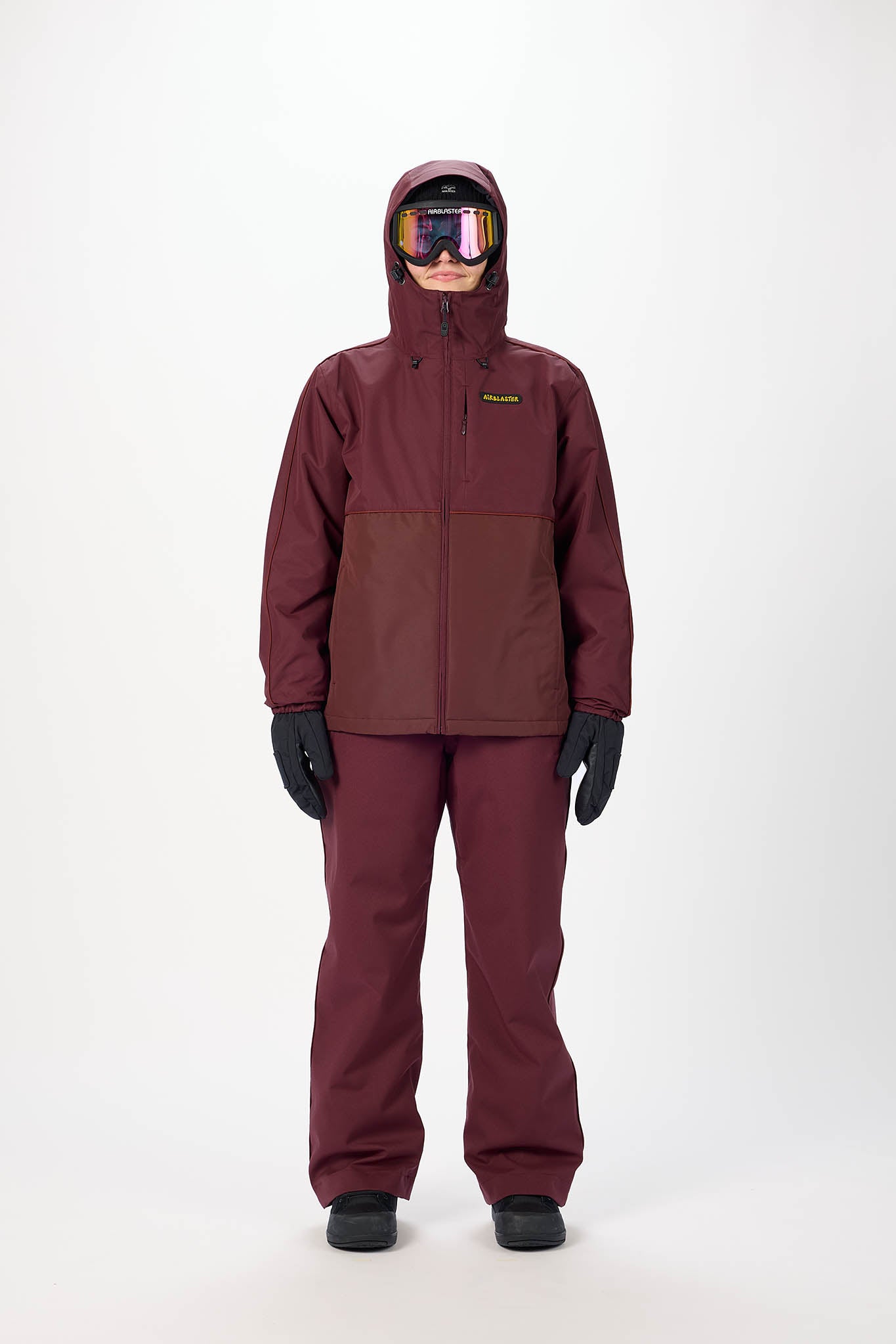 Person wearing a maroon snowsuit with goggles on a white background